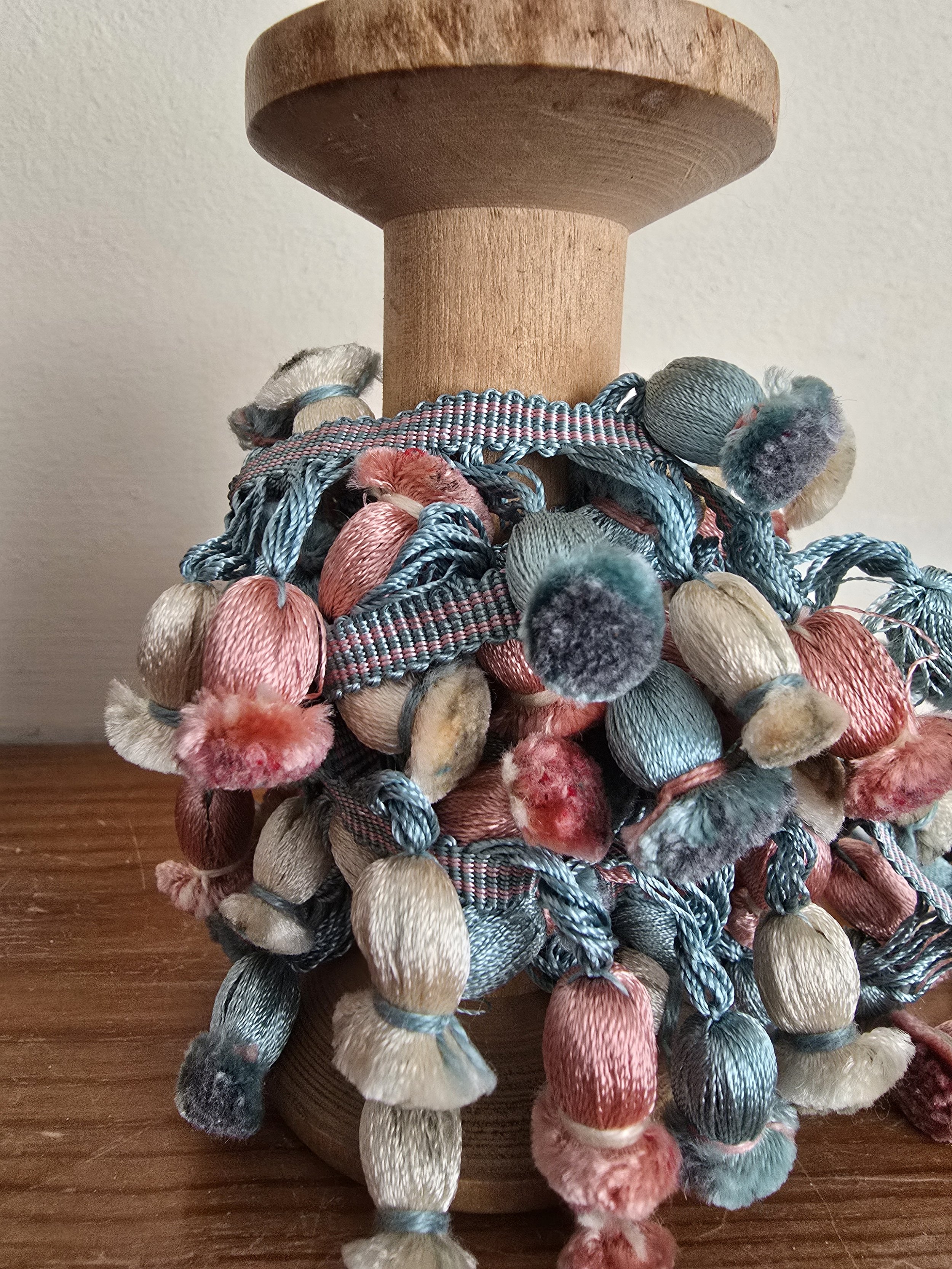 close-up of pastel trim with velvet-tipped tassels in rose, cream, and blue on antique spool