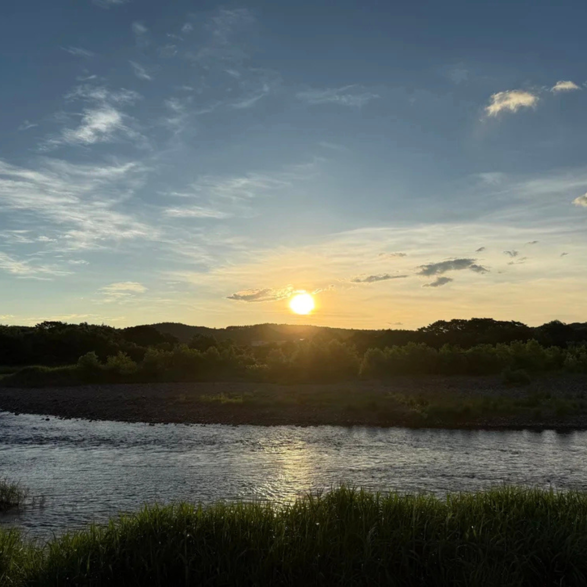 Evening sunlight glimmers across a slow-moving river as the day draws to a close. The horizon glows in shades of gold and blue, while trees and distant hills settle into shadow, capturing a quiet moment of reflection in the natural world.