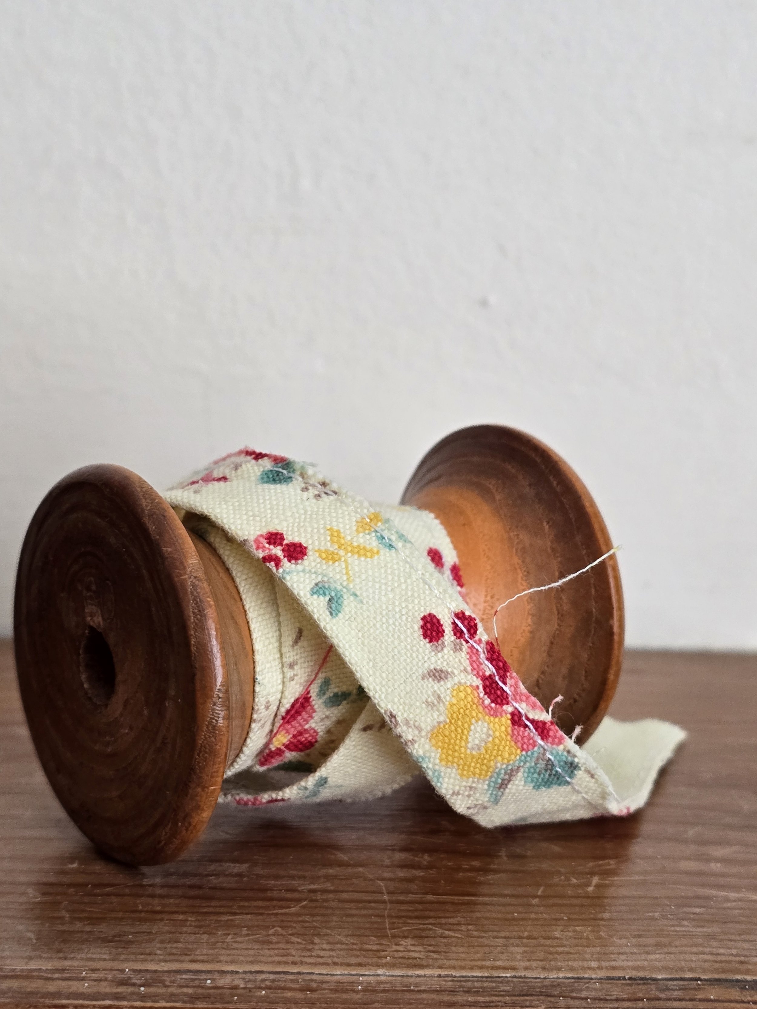 Side view of antique French floral ribbon, faded with time, on original spool