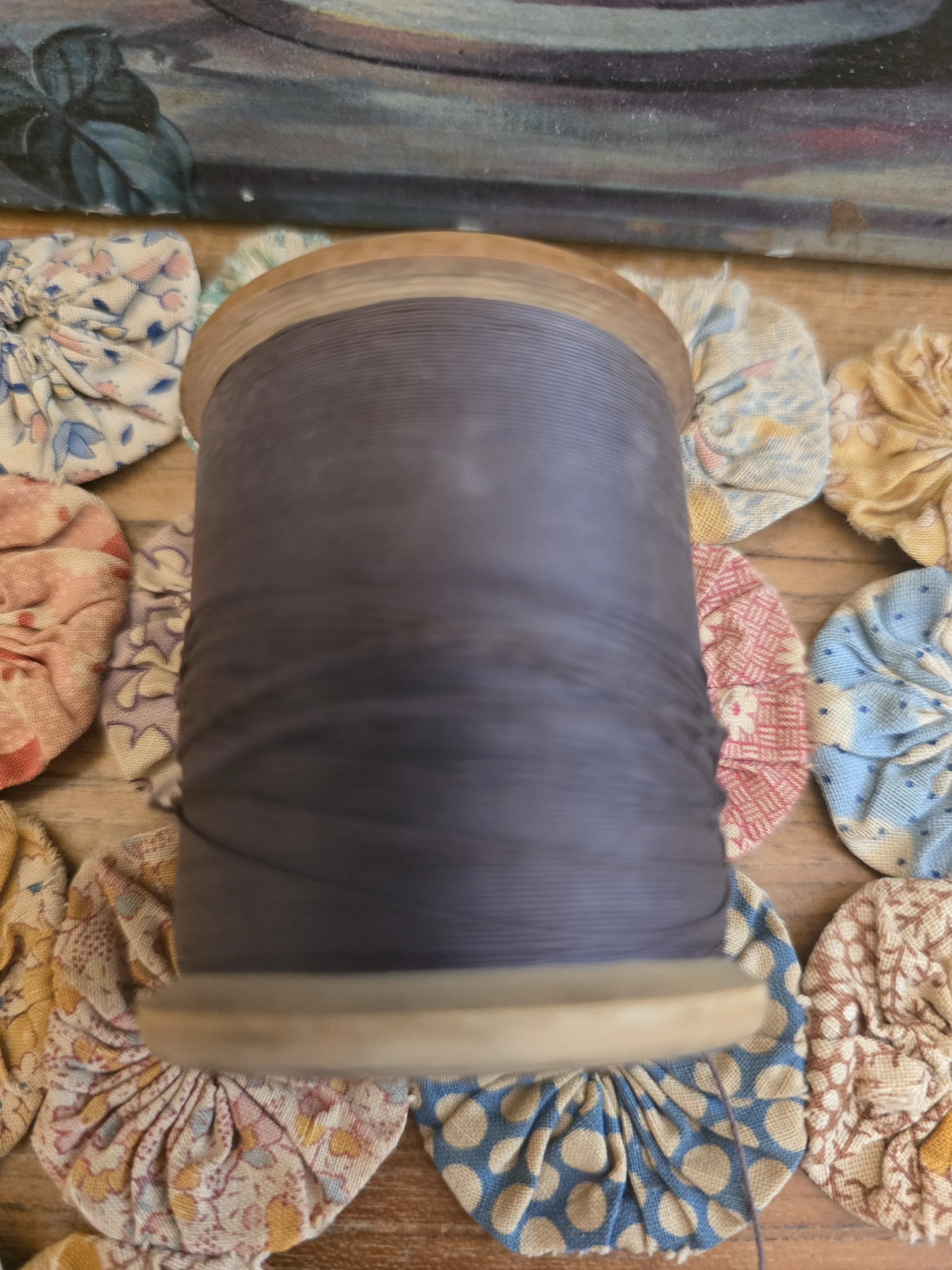 Vintage haberdashery spool displayed among fabric yo-yo flowers, featuring original thread and aged wooden ends