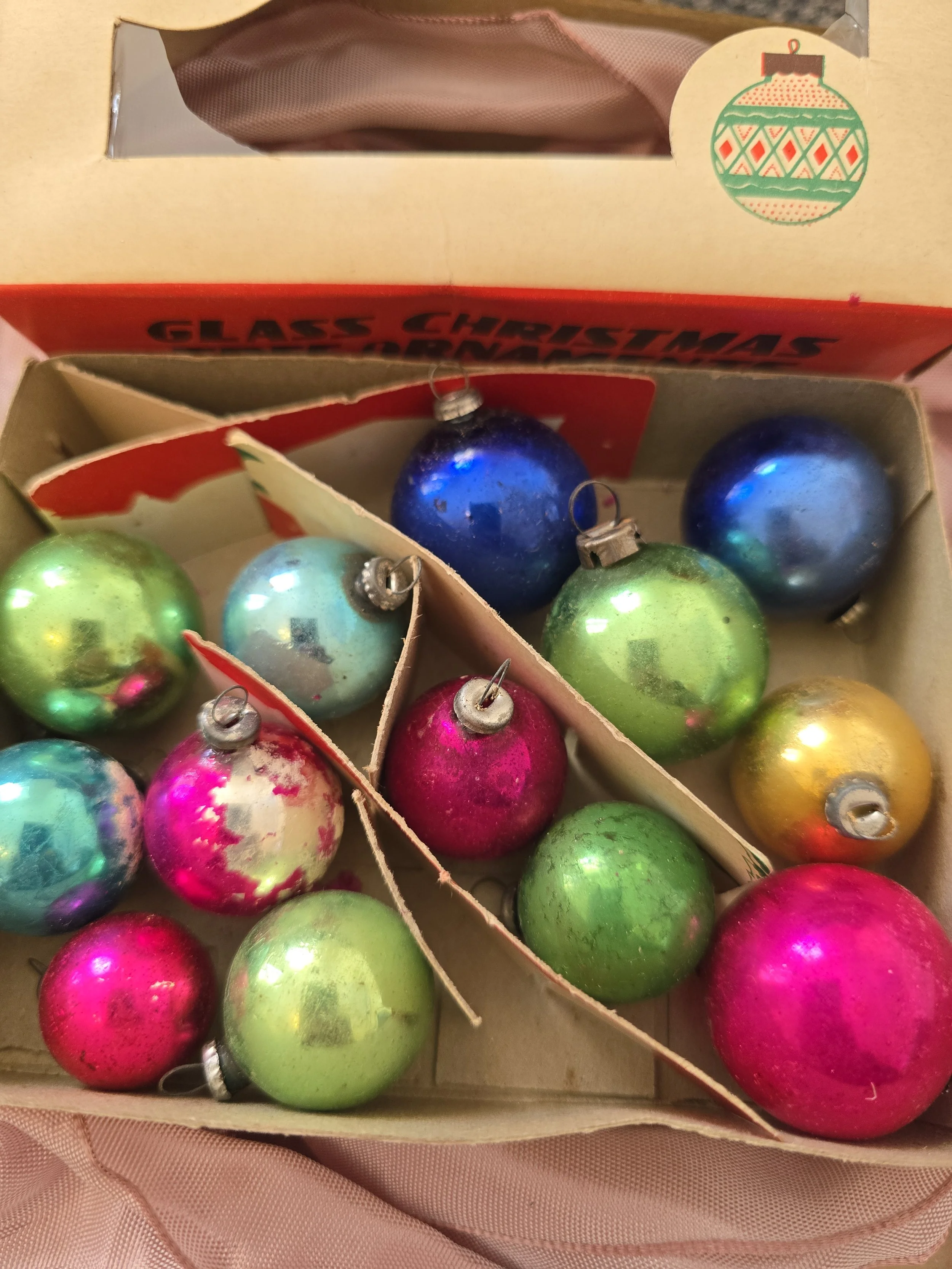 Assorted small vintage glass Christmas baubles in pink, blue, green and gold, arranged inside an old Woolworth cardboard box.