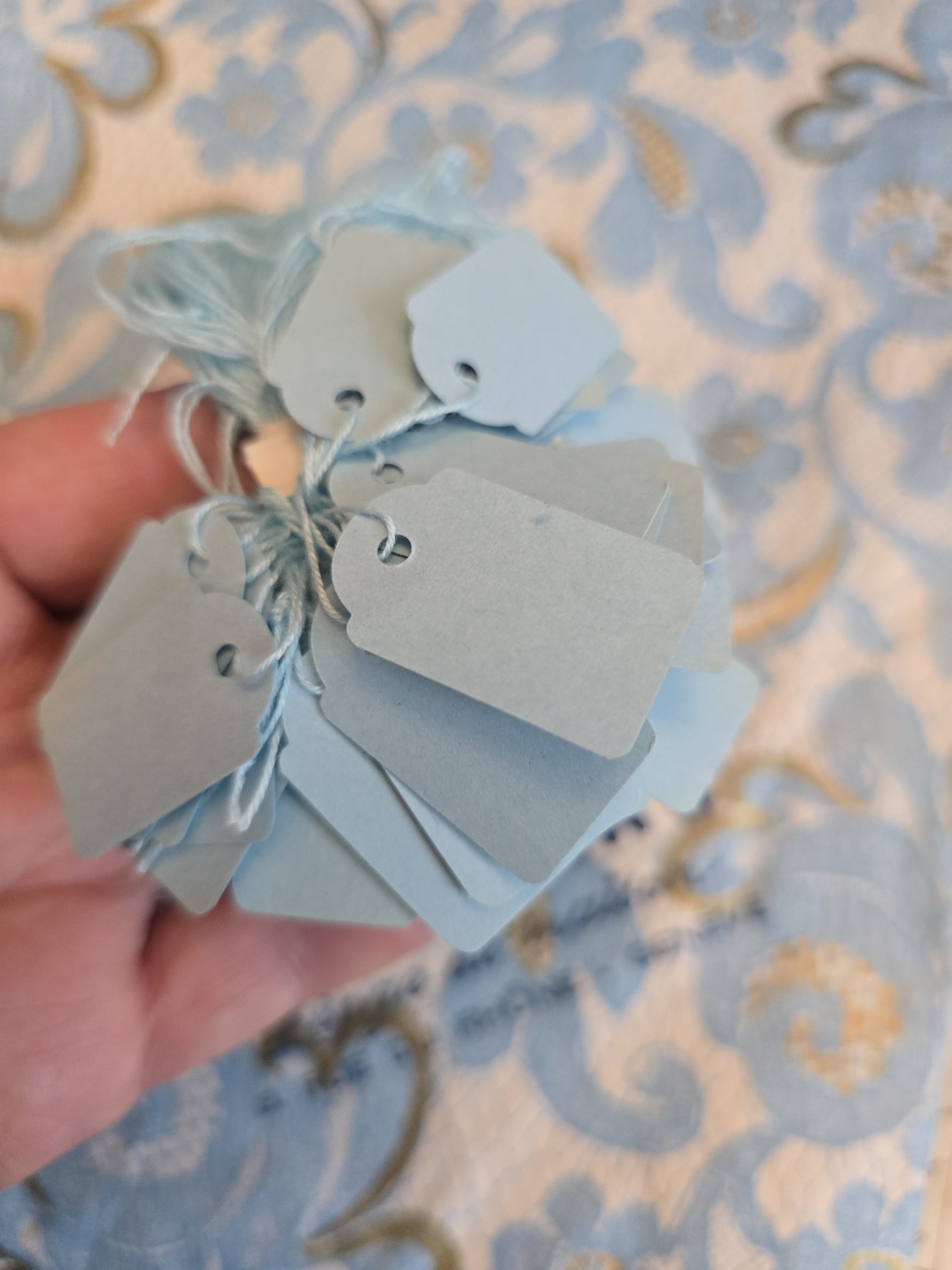 Close-up of a bundle of small vintage French paper price tags in several shapes and soft powder blue shades.