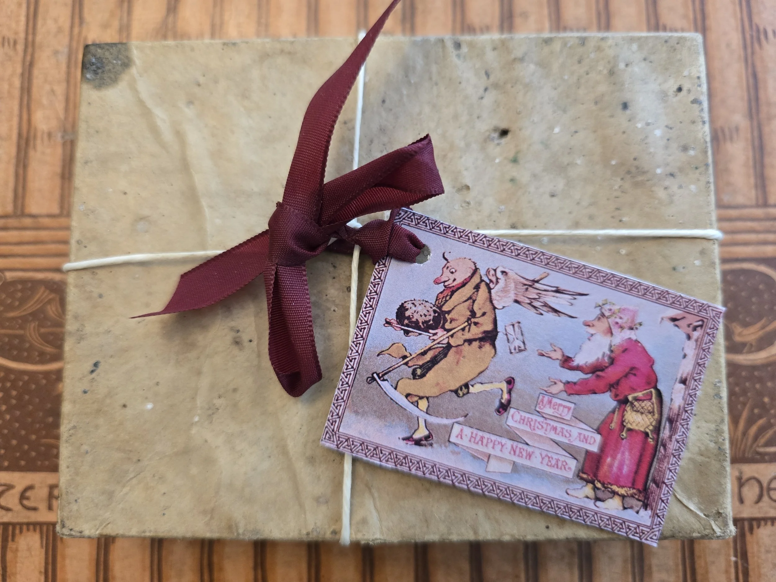 Printable antique Christmas gift tag tied with burgundy ribbon to an old paper-wrapped book.