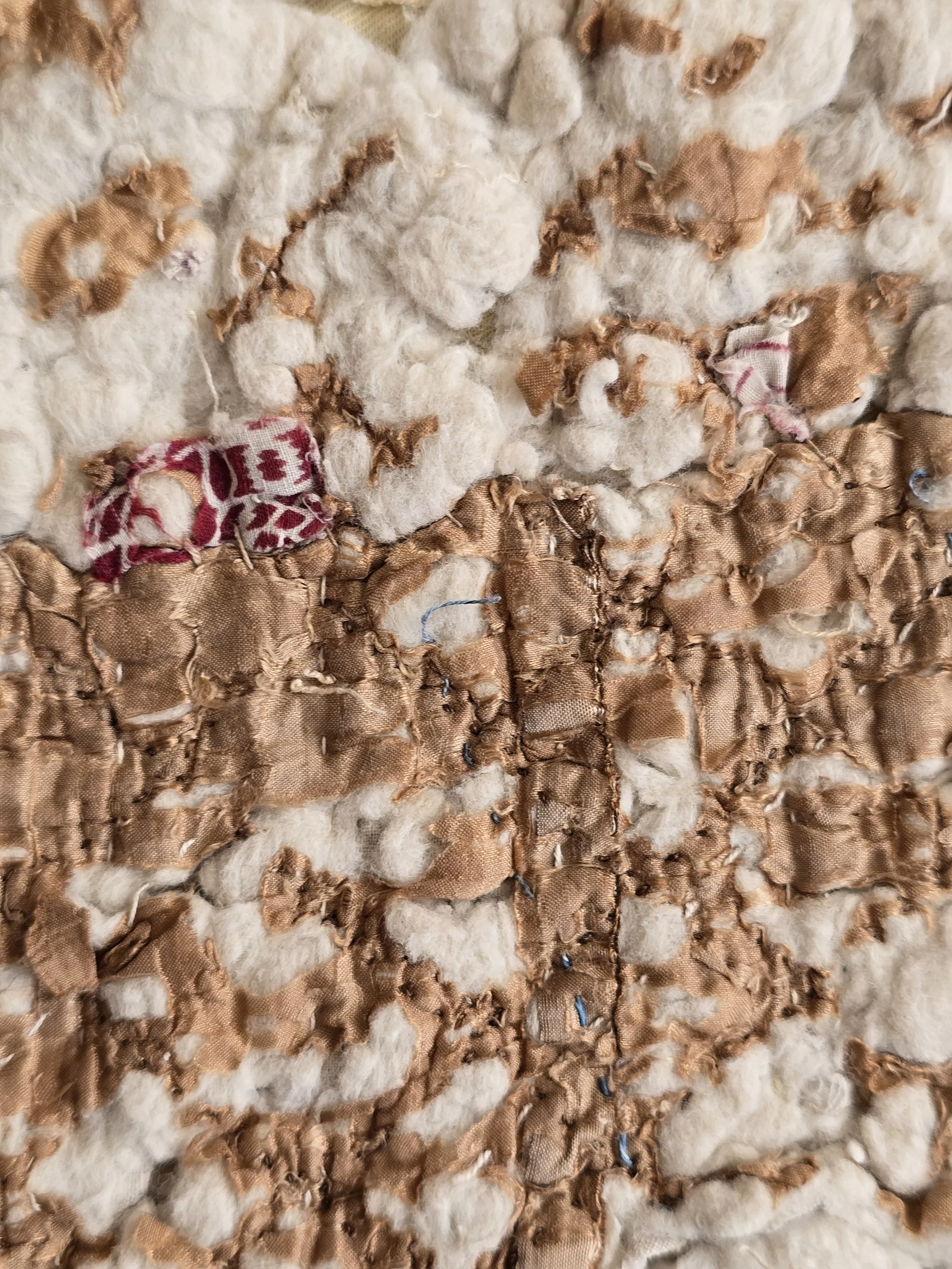 Close-up of distressed antique quilt with fragmented tan textile, wadding and old hand stitching.