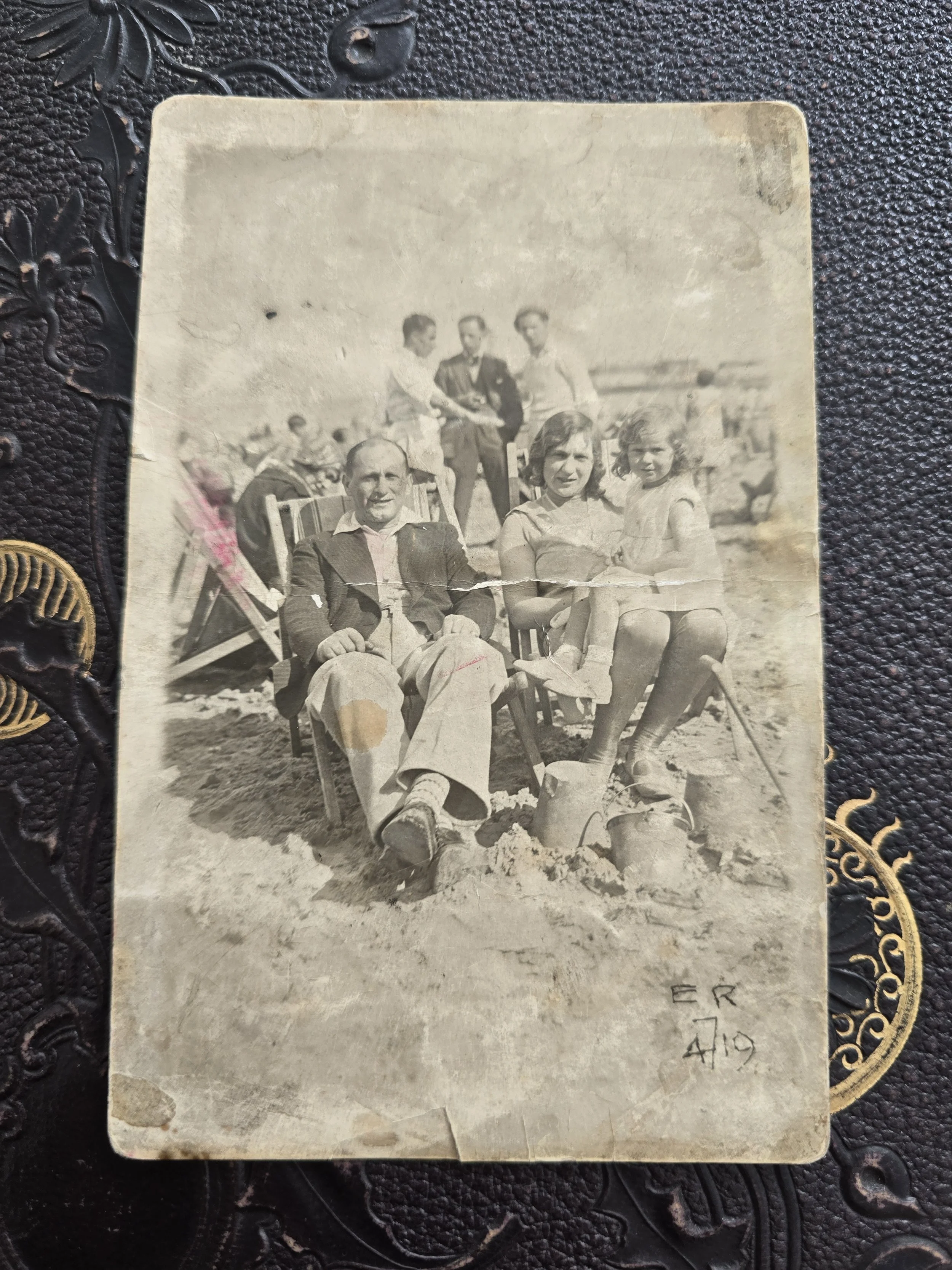 Original 1930s seaside family photograph showing a man, woman and young girl sitting in deckchairs on the beach.