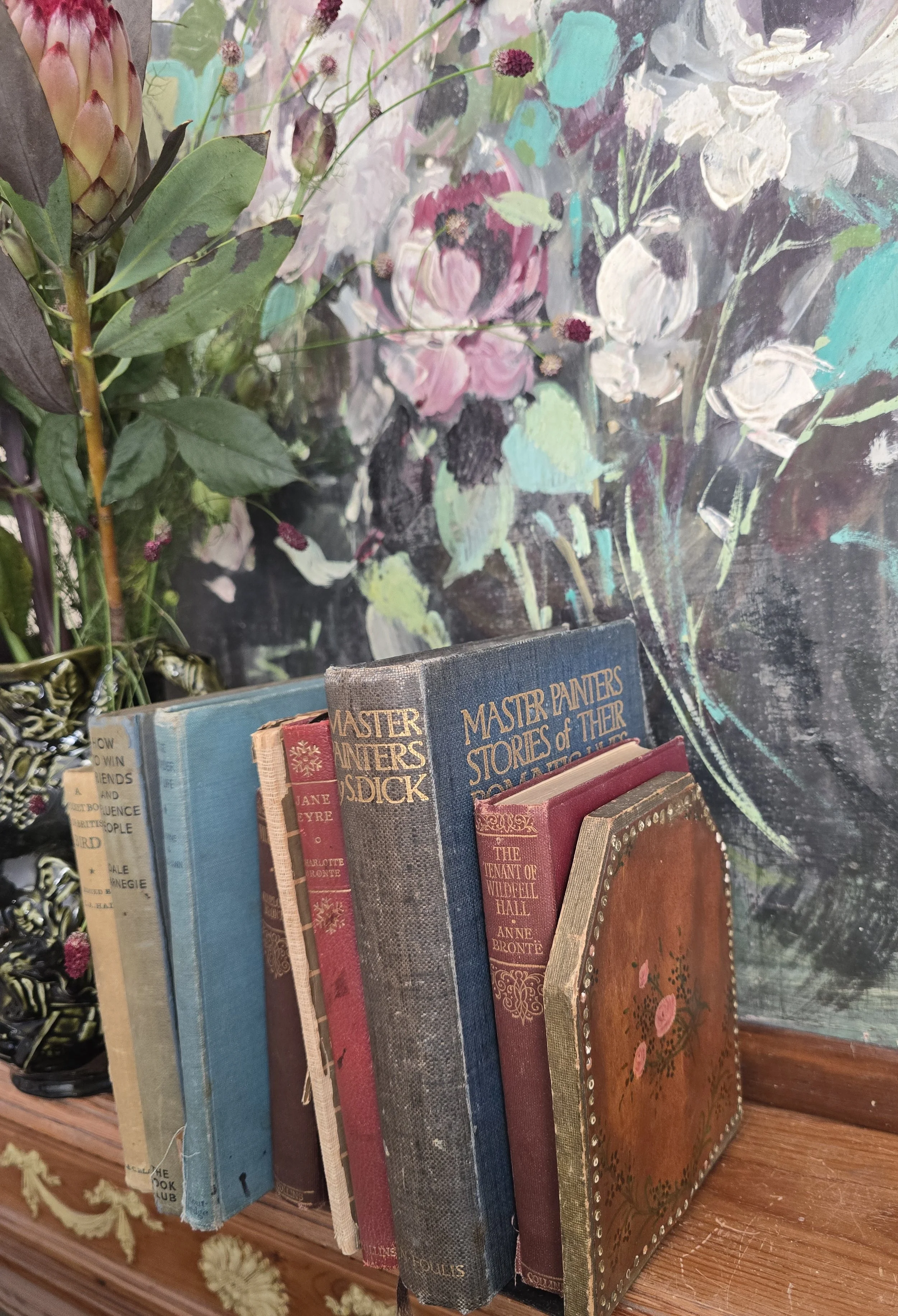 Angled close-up of vintage floral leather bookend pressed against hardback books, showing wear and detailed hand painting.