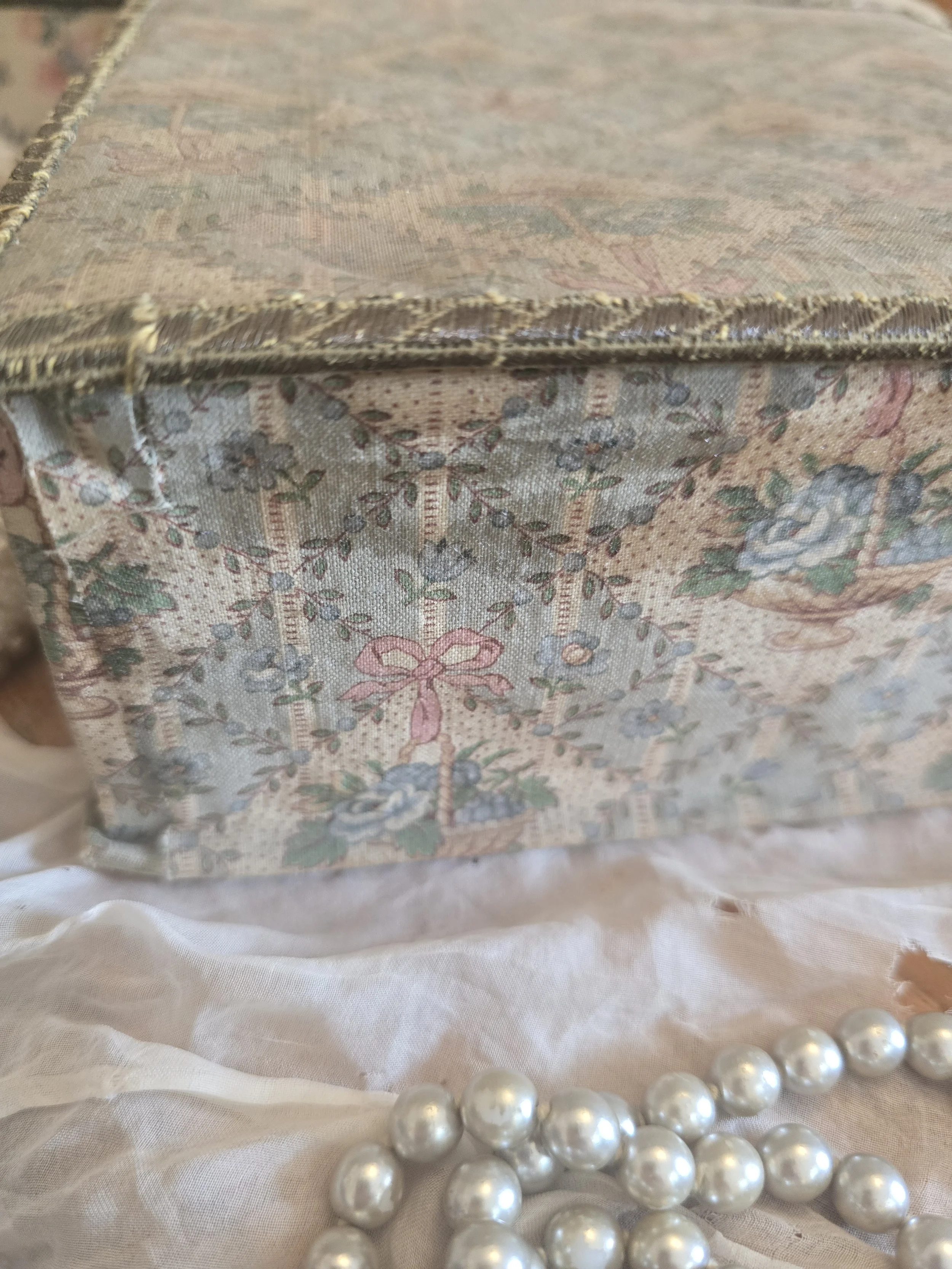 Close-up of timeworn metallic trim and faded floral textile covering on antique French box.