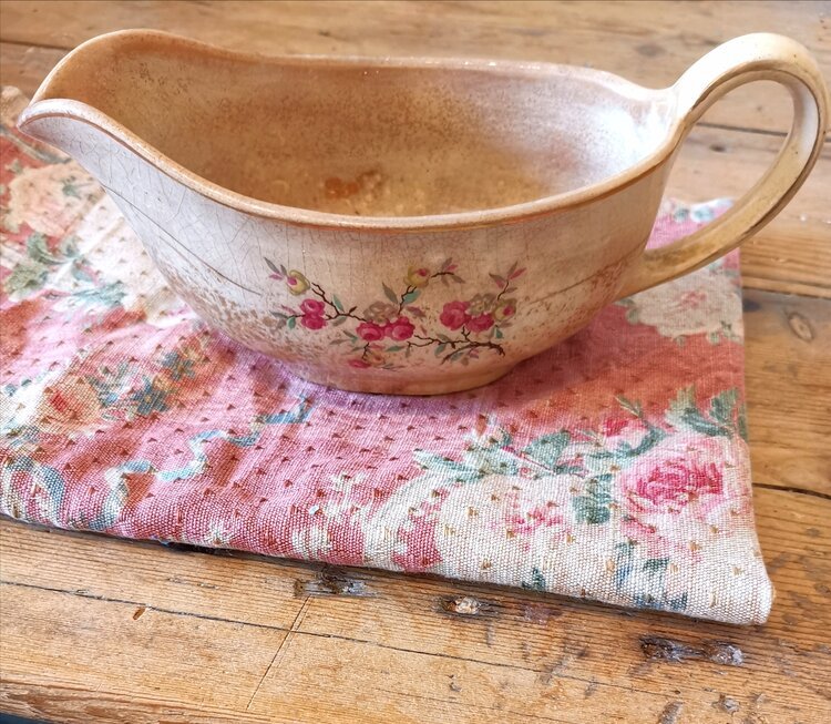 Side view of a French antique ceramic sauce boat with floral pattern, resting on vintage pink cloth