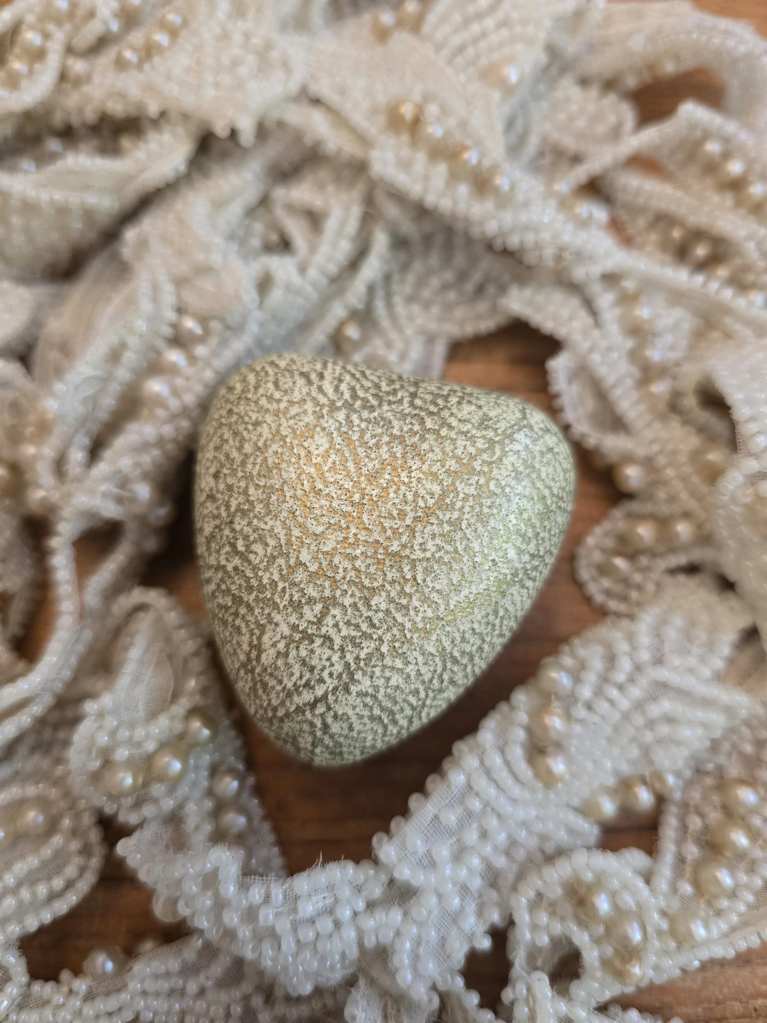 Vintage heart shaped ring box with textured pale green exterior resting on antique beaded lace.