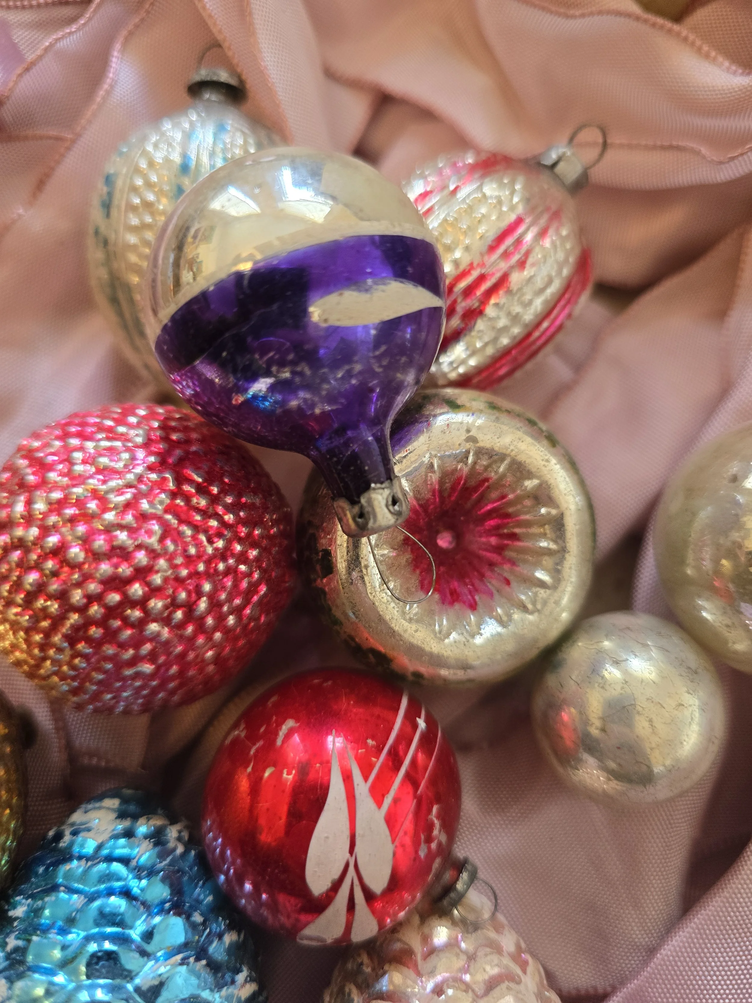 Close-up of old silvered glass Christmas ornaments showing faded green decoration, worn finishes and metal hanging fittings.