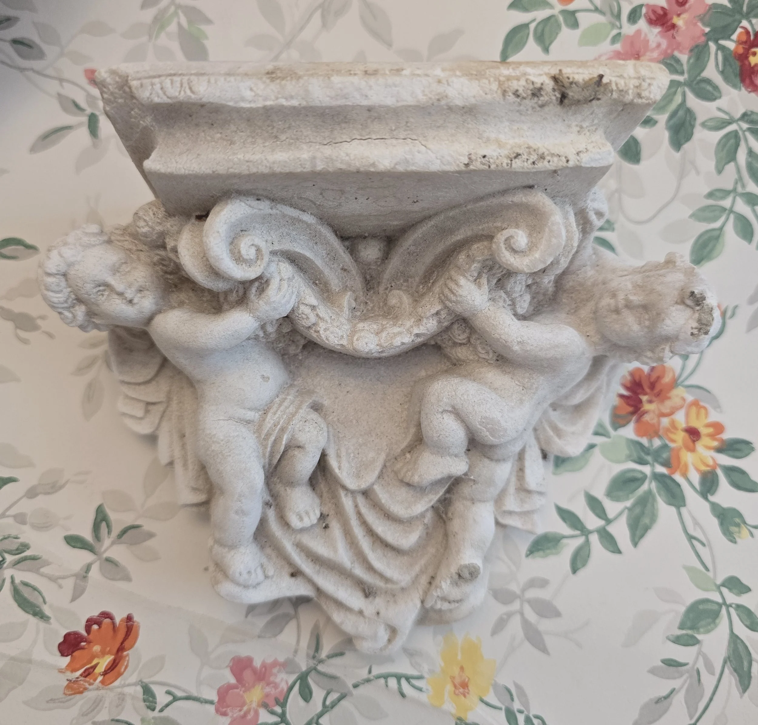Antique wall bracket featuring two winged cherubs supporting an ornate shelf.