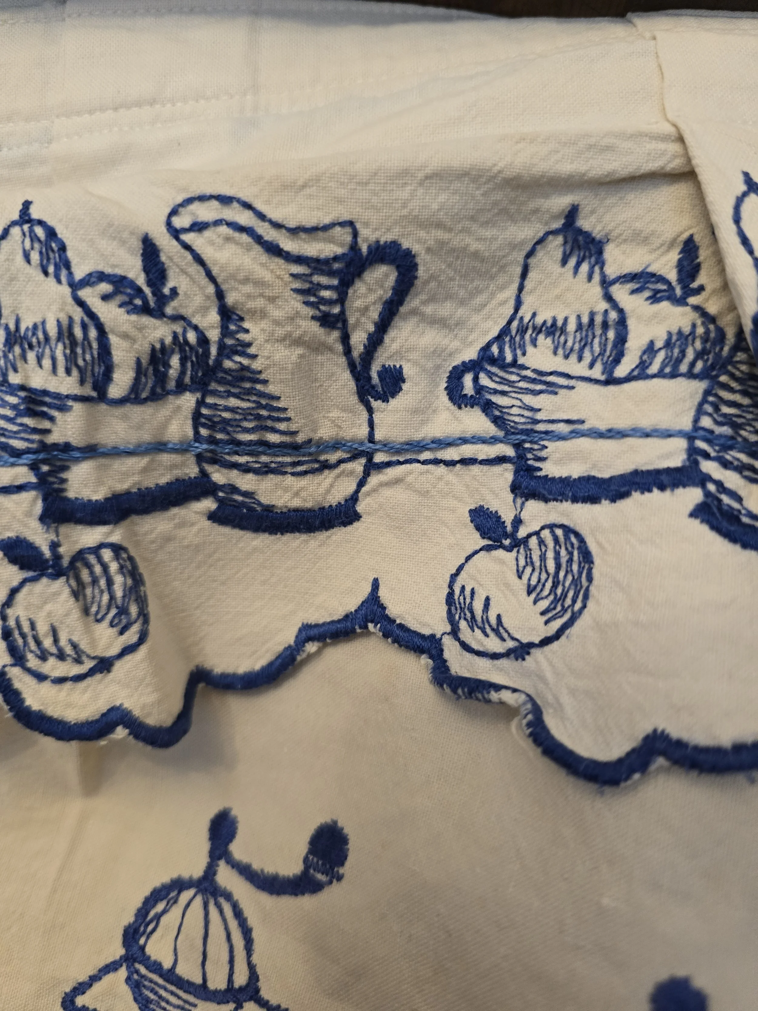 Vintage white kitchen curtain valance with scalloped blue embroidered border and repeated coffee grinder illustrations.