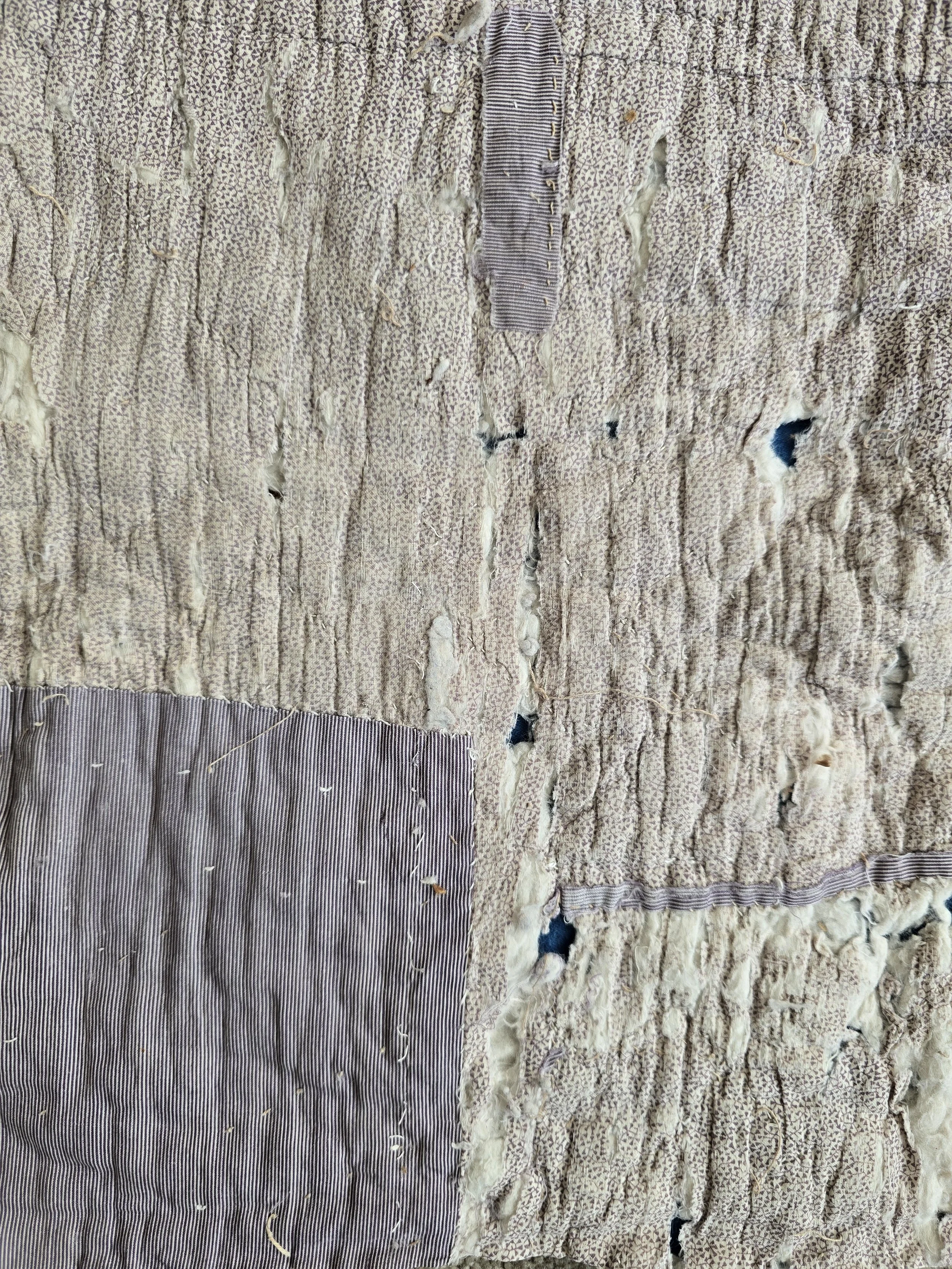 Antique French quilt fragment with faded purple printed cotton and exposed layers.