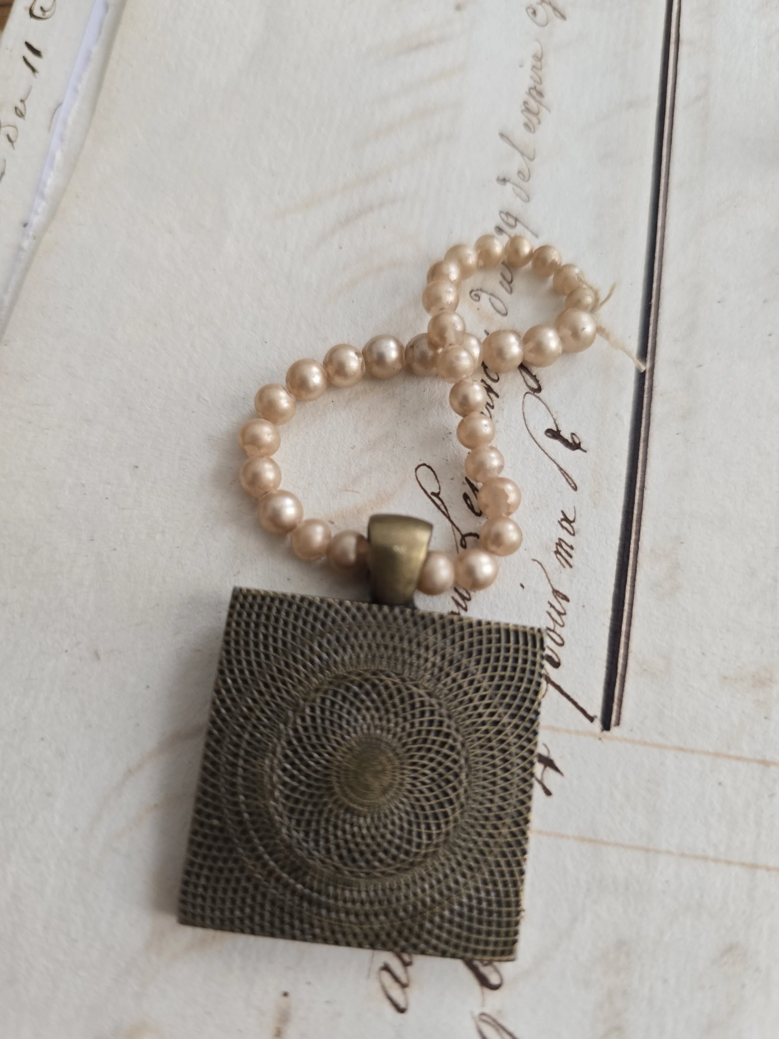 Small handmade portrait pendant displayed on antique handwritten paper.