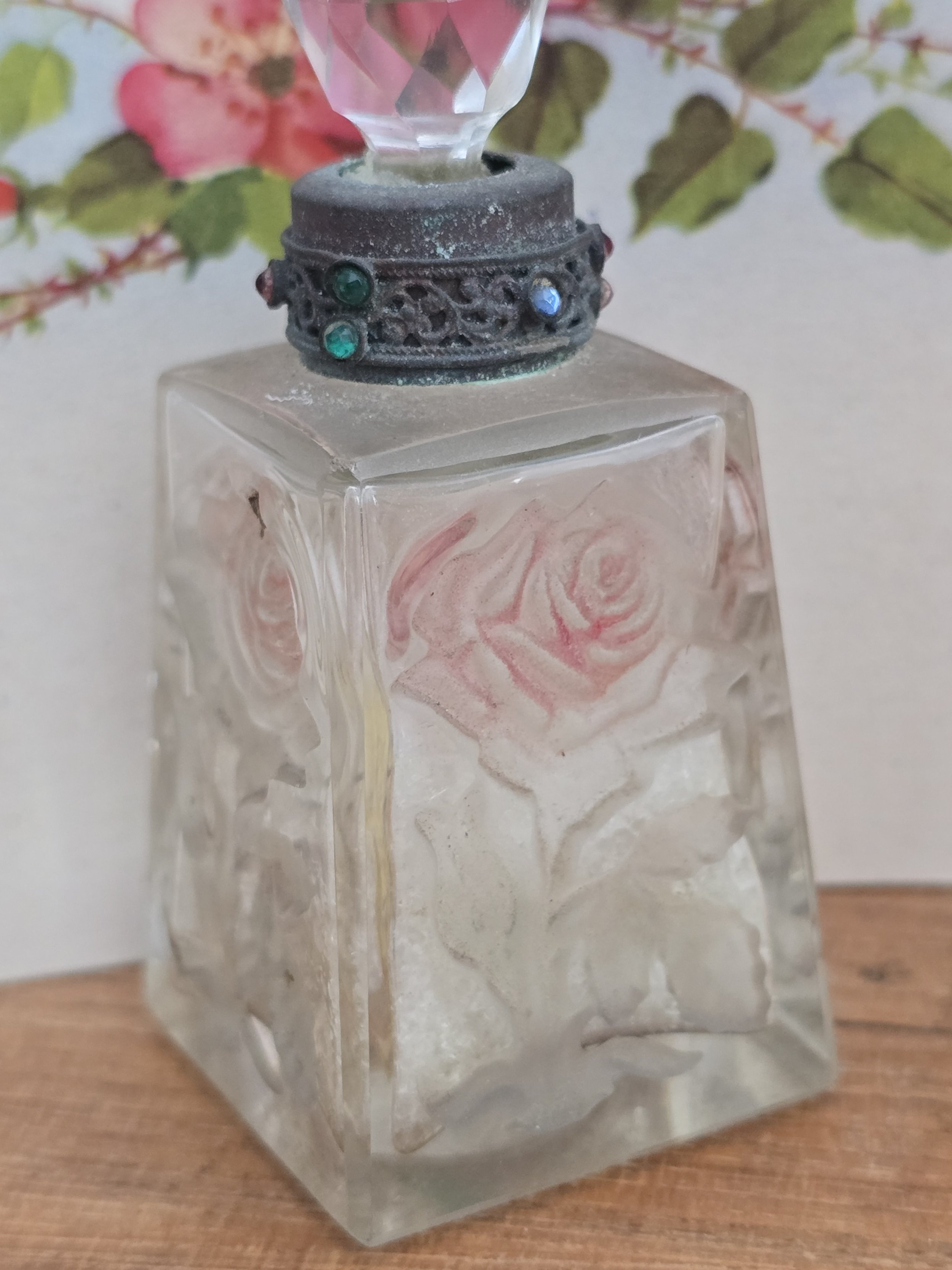 Side view of an antique frosted glass perfume bottle showing raised pink rose decoration.