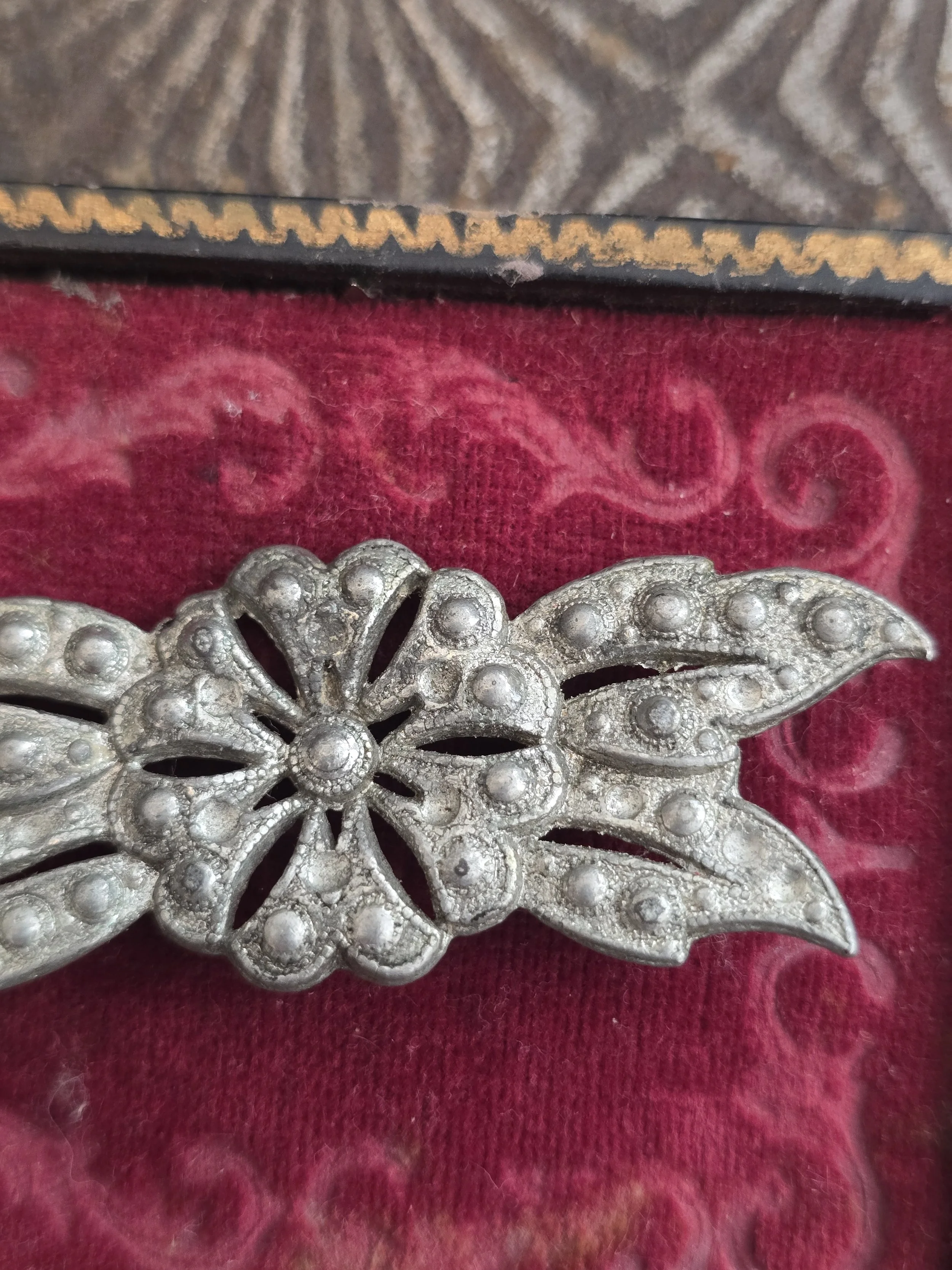 Close-up detail of a vintage floral brooch showing raised bead decoration and aged silver-tone finish.