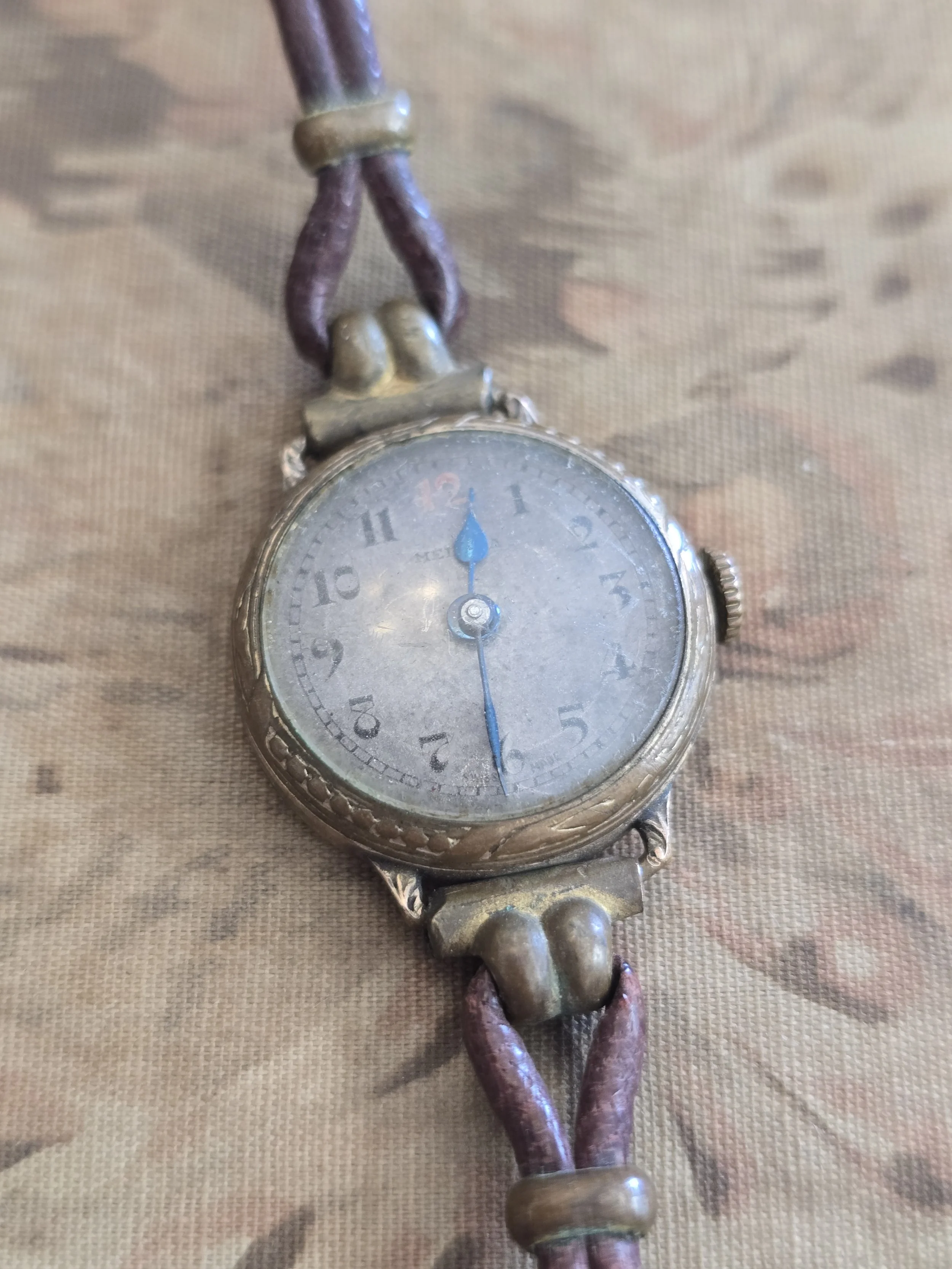 Decorative antique wristwatch showing timeworn dial and brass-toned case details.