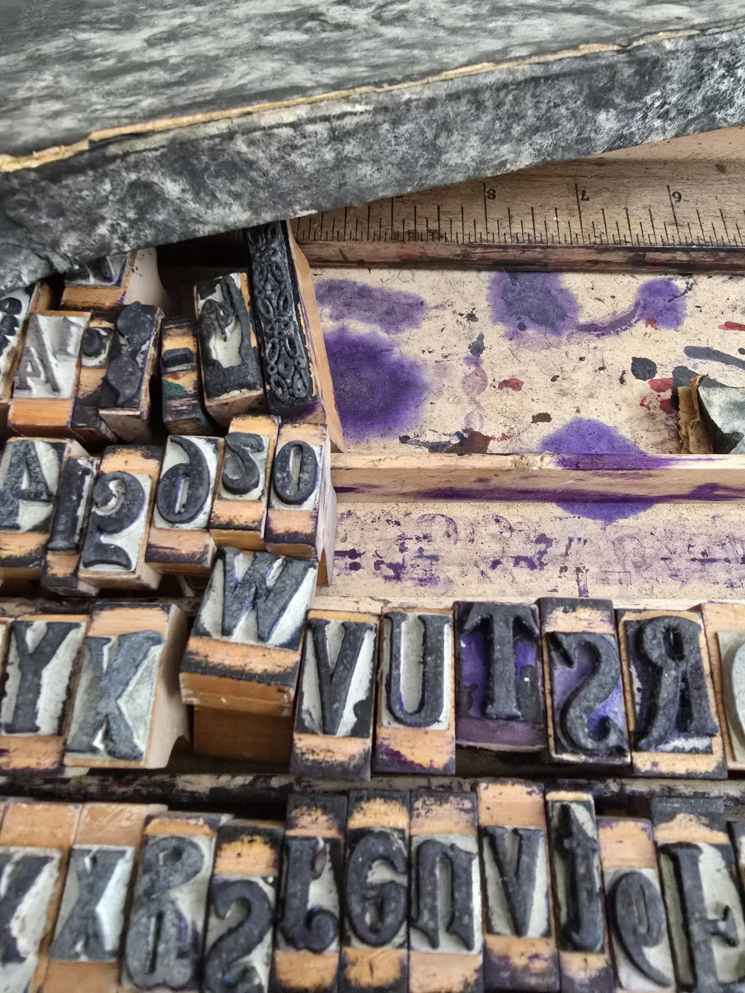 Ink-stained vintage wooden case holding rubber stamp letters and numbers.