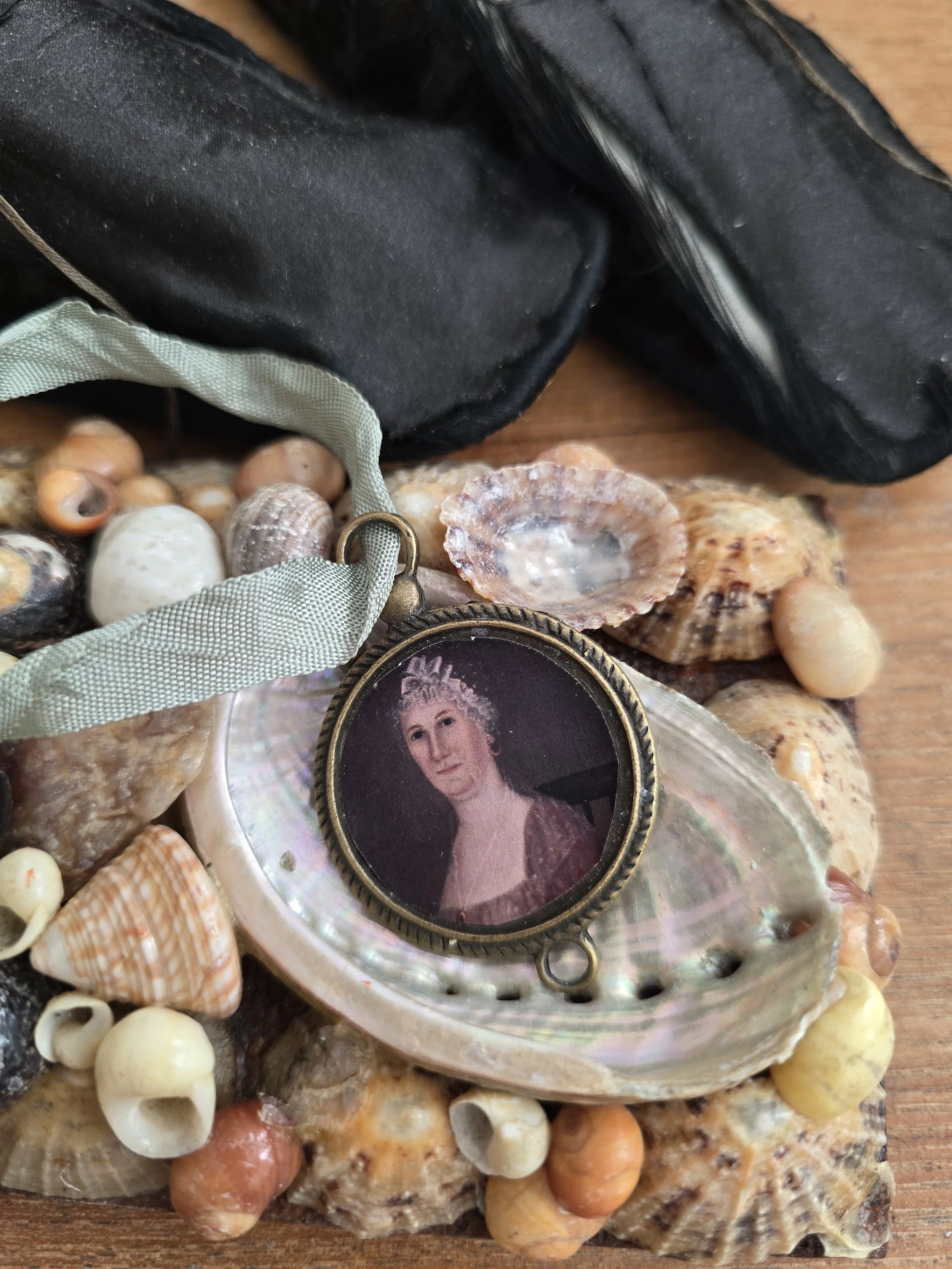 Studio Made decorative portrait hanging with vintage sage green ribbon, displayed amongst a collection of old seashells.