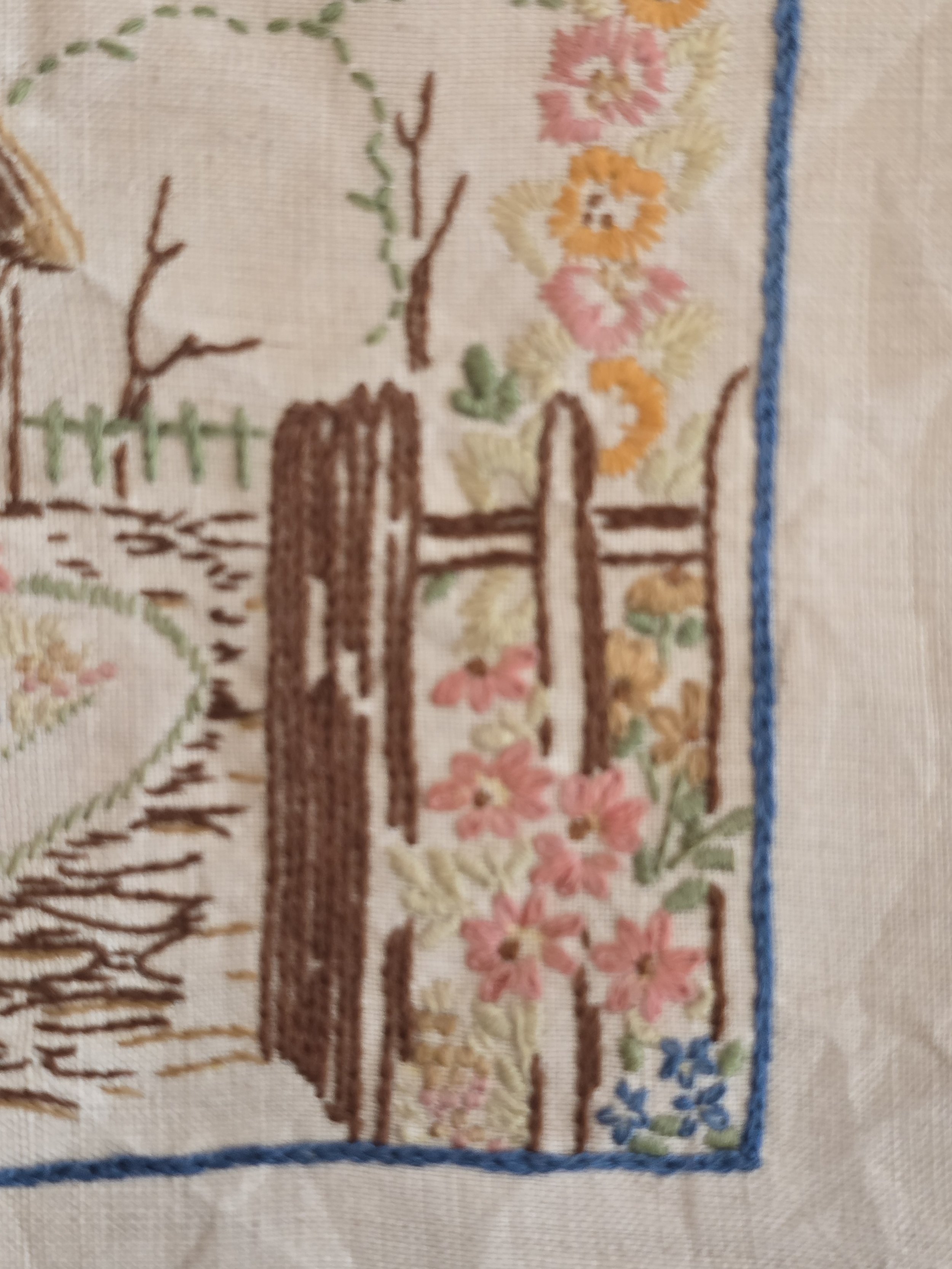 Embroidered picket fence and garden gate within a cottage garden scene.