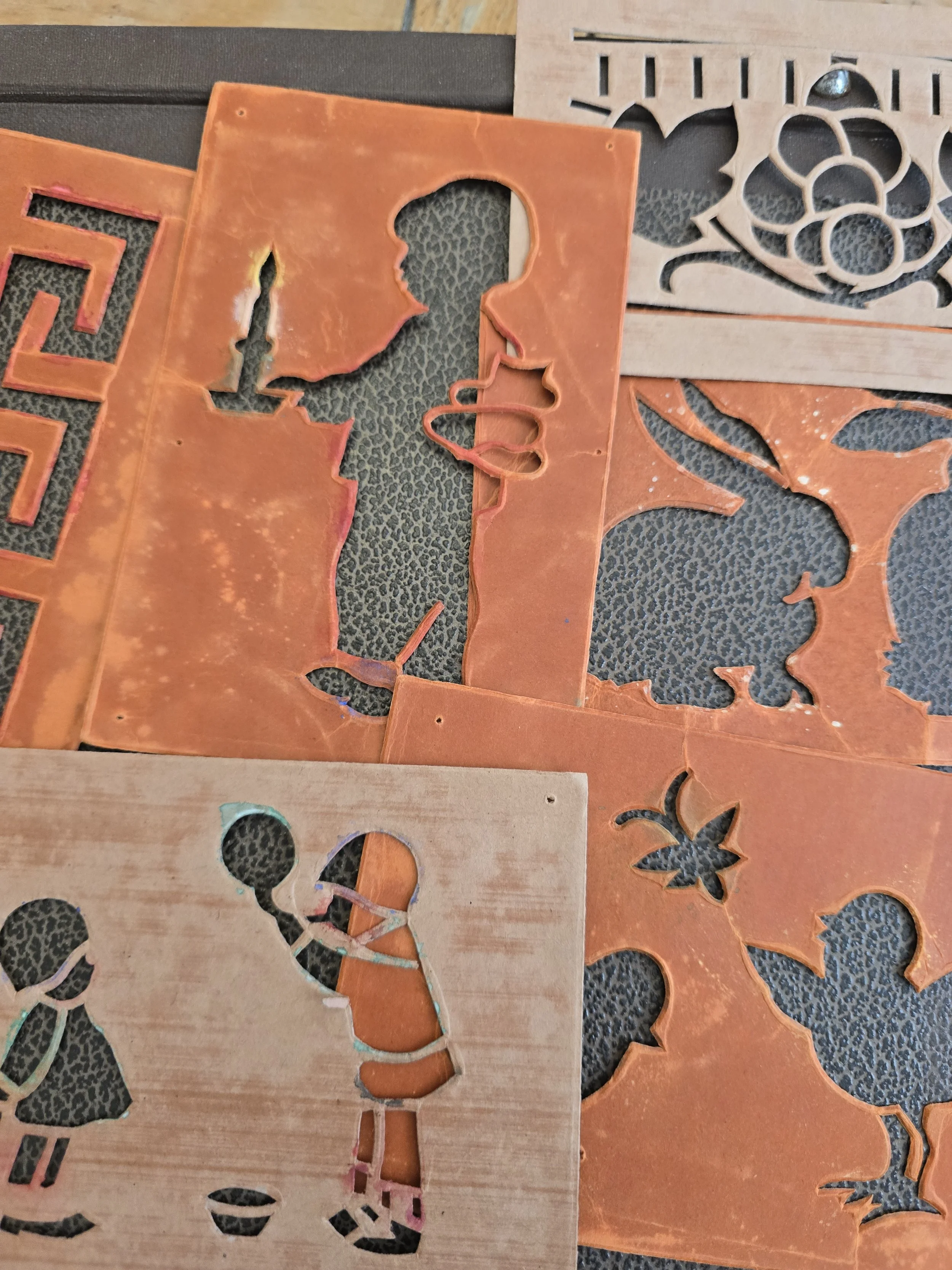 Close-up of early 20th-century children's card stencil designs showing little figures in period clothing with traces of coloured paint.