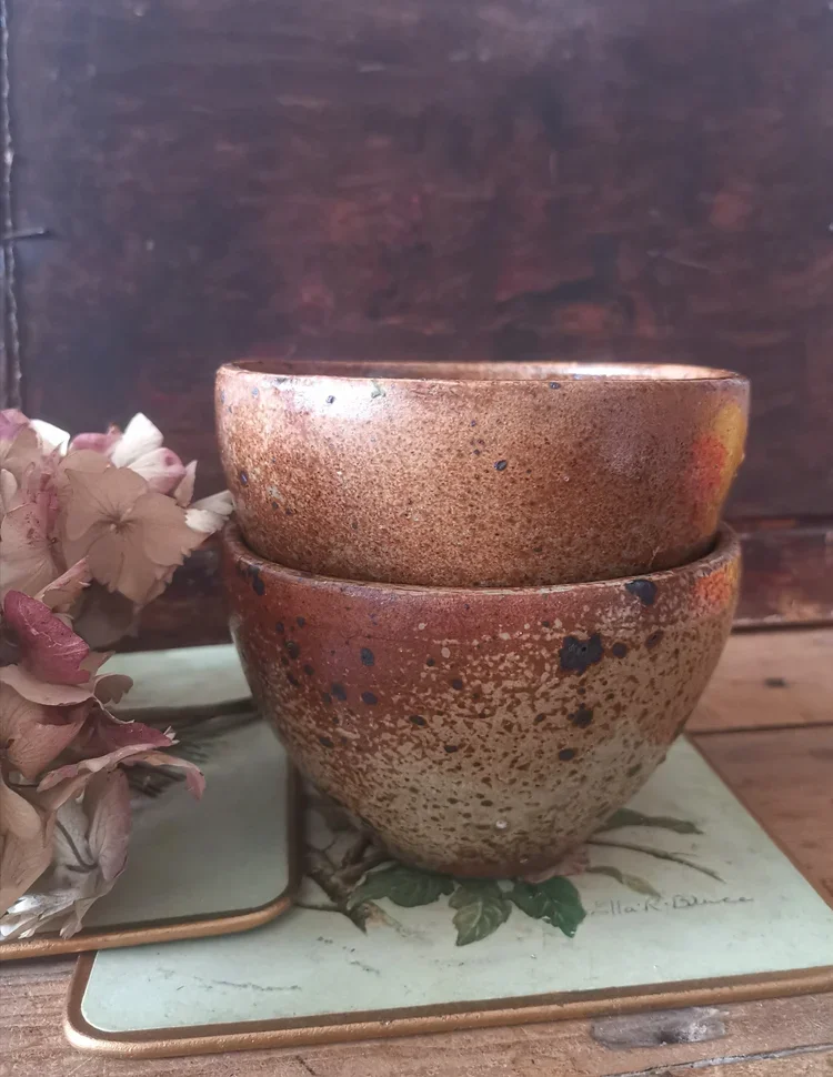 Stacked side view of vintage rust-glazed French bowls with floral coaster and dried flowers.