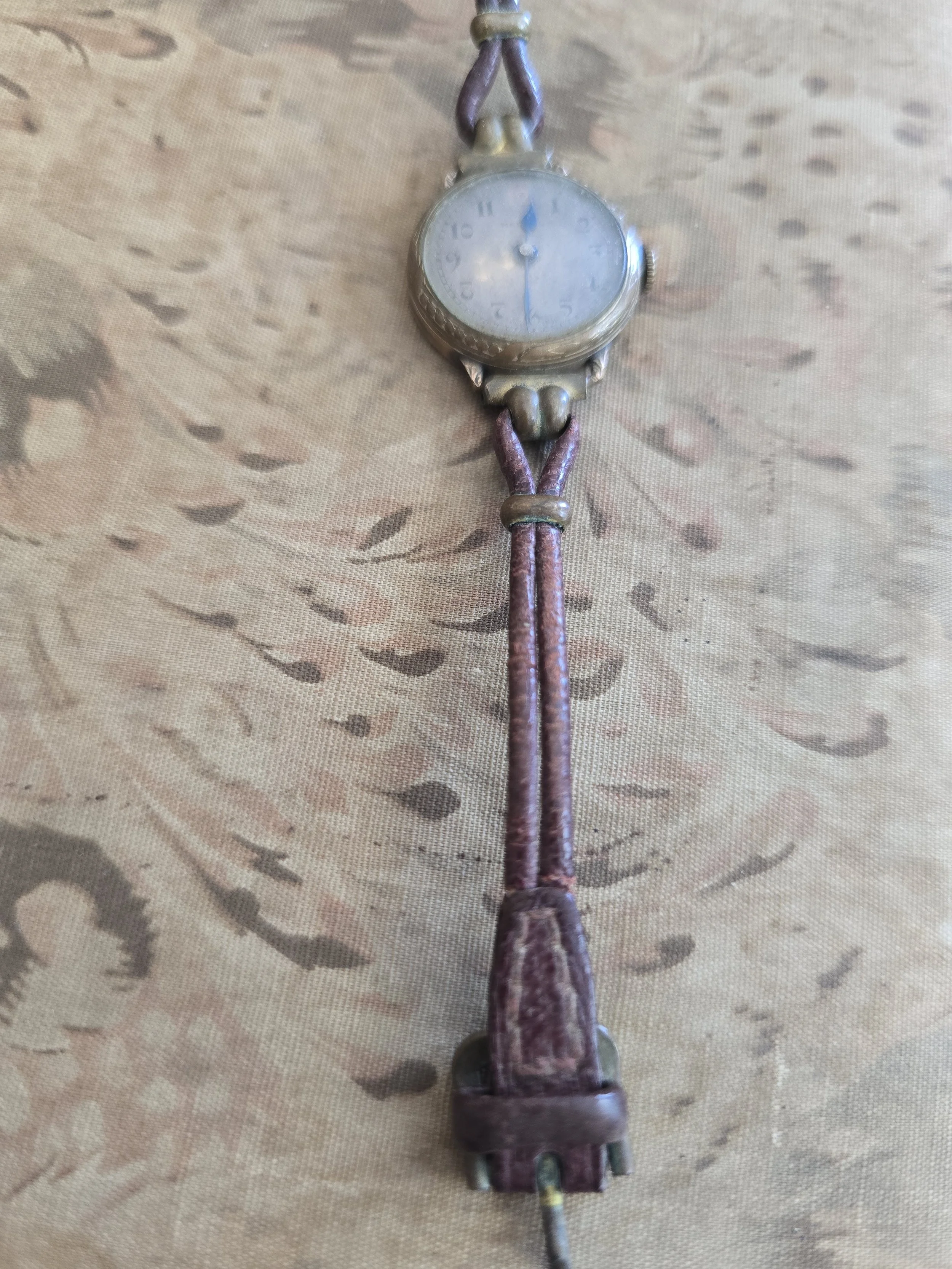 Side view of vintage wristwatch with worn original cord strap and fittings.