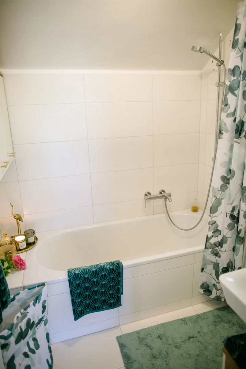 Ein Badezimmer mit einer Badewanne, einer grünen Badewanne-Handtuch, einer Dusche mit Duschvorhang, Kerzen, einer Pflanze und einem grünen Badteppich.