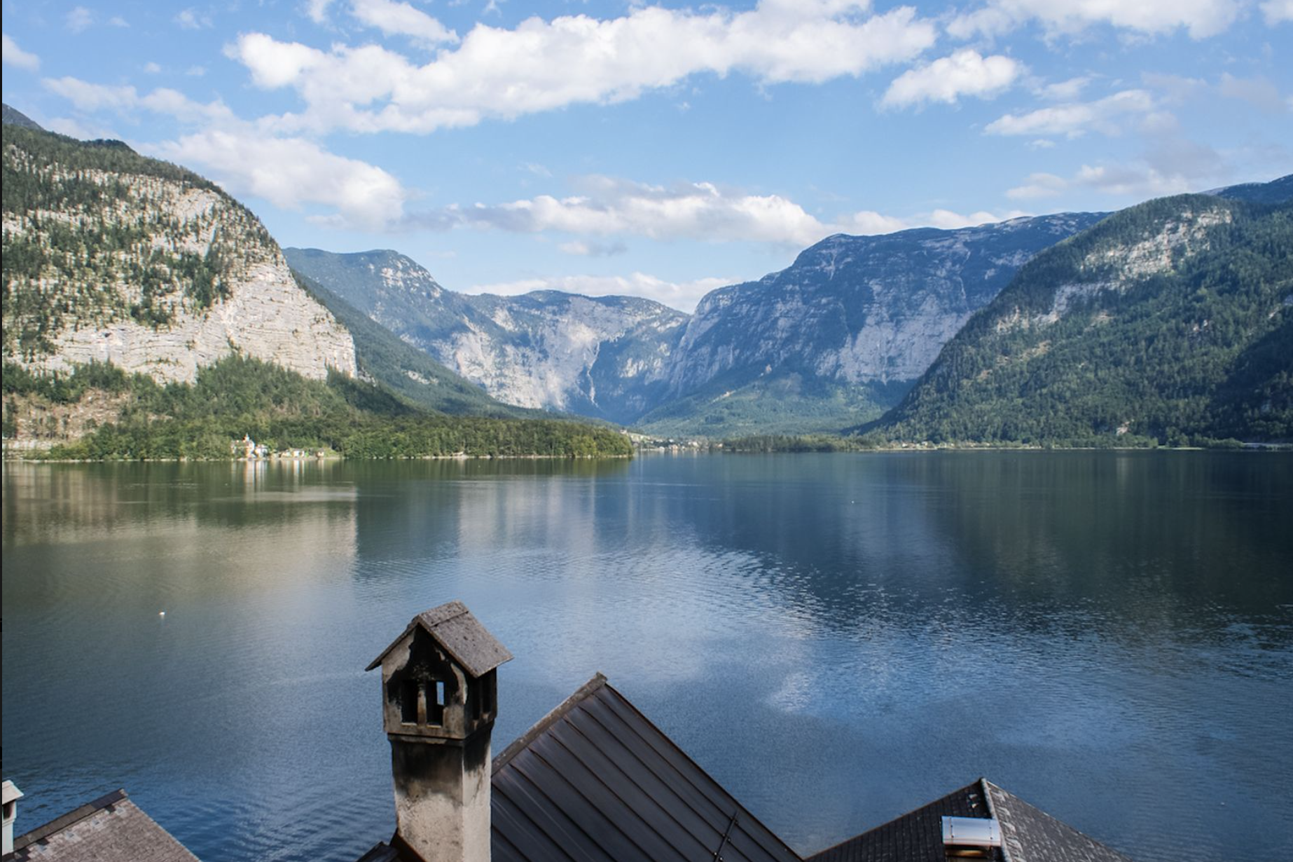 Ausblick von Wohnzimmer auf den Hallstätter See. Blick auf einen See mit Bergen im Hintergrund und Häusern im Vordergrund.