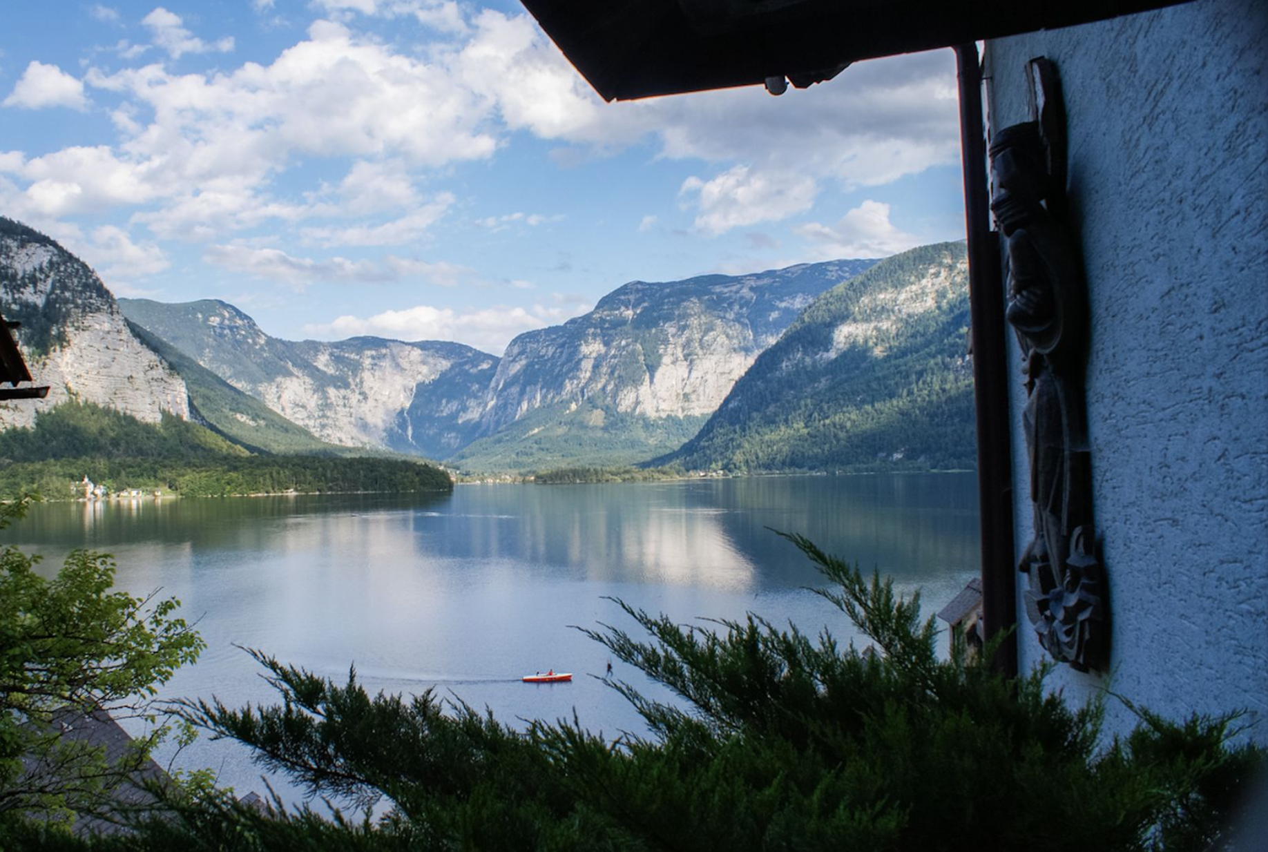 Blick von einer Terrasse auf einen ruhigen Hallstätter See, umgeben von hohen, bewaldeten Bergen unter einem blauen Himmel mit Wolken.
