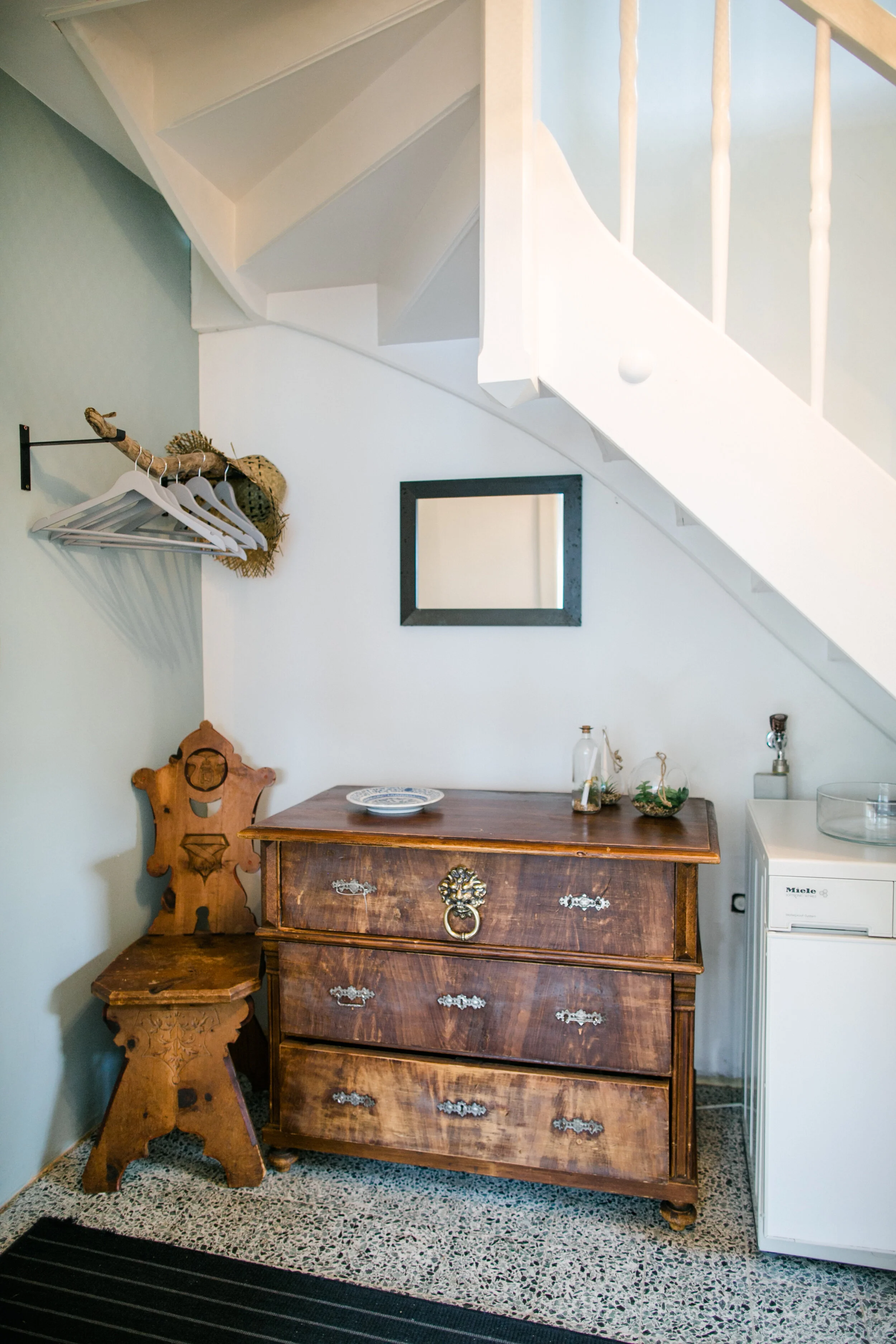 Traditionelle Kommode, ein Spiegel und ein kleines Regal unter einer Treppe in einem Raum.
