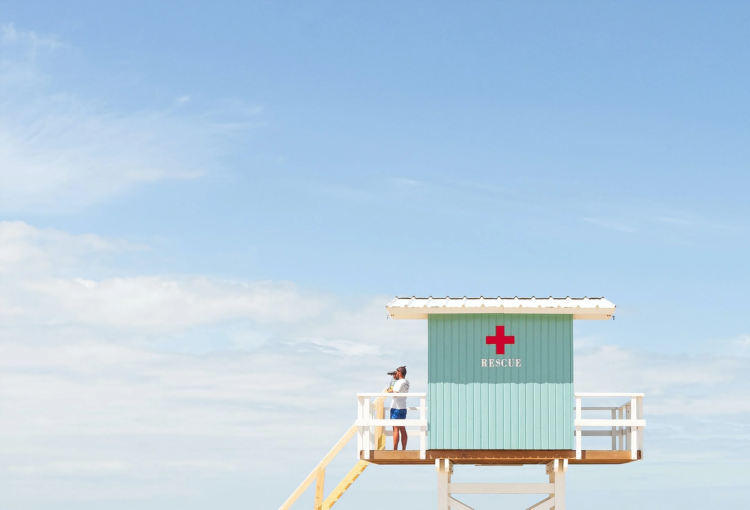 Lifeguard tower with a rescue sign, lifeguard using binoculars, clear blue sky.