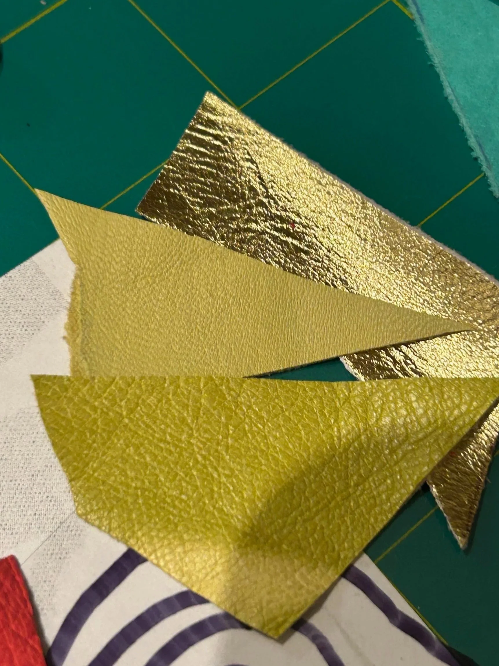 Close-up of shiny gold and metallic leather in various textures, layered on top of a work board.