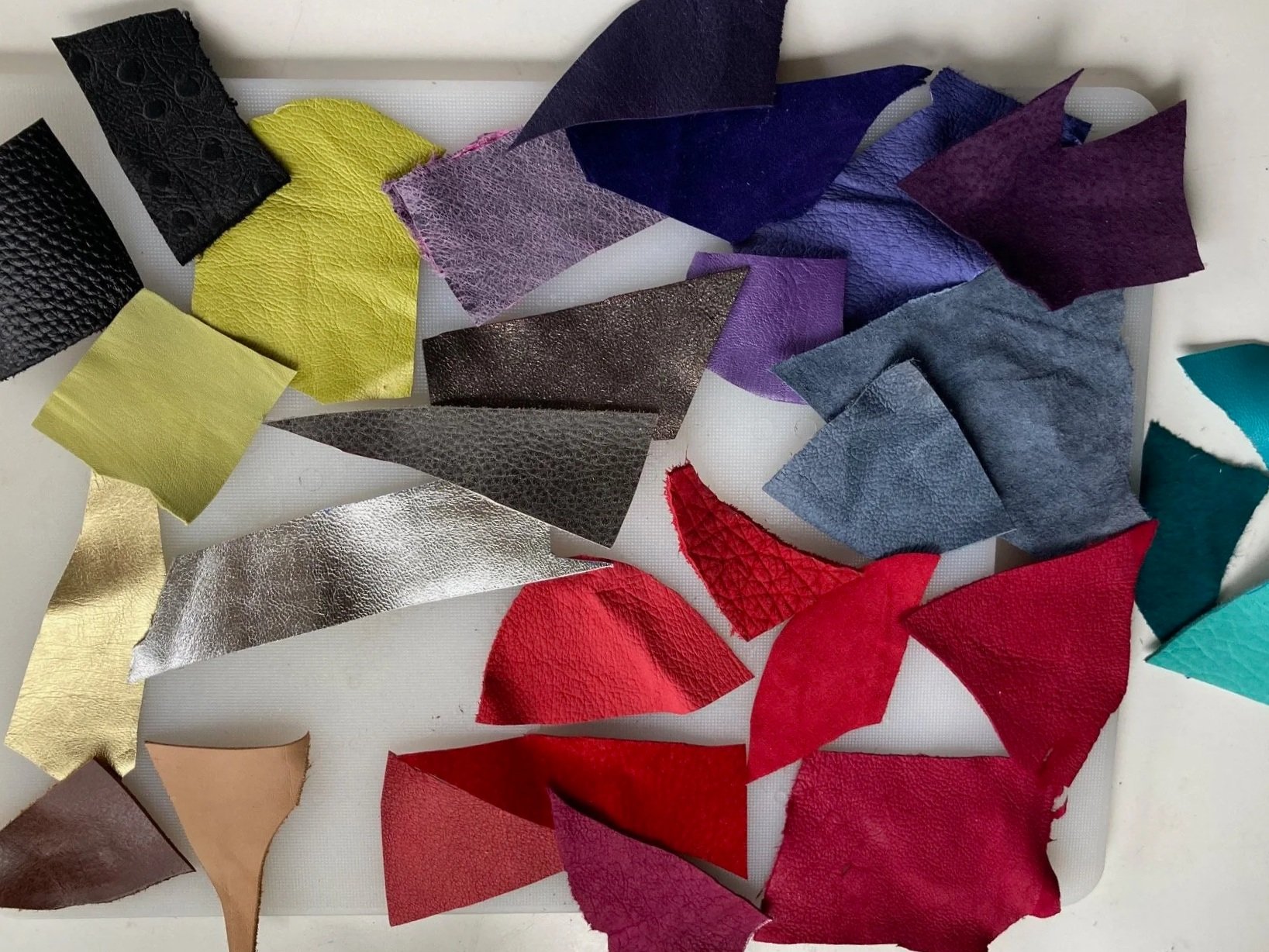 Assorted pieces of leather in a wide variety of colorus and textures arranged on a white surface.