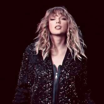 A woman with blonde hair wearing a black, studded jacket against a dark background.