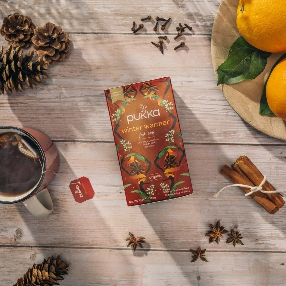 A flat lay of a Pukka Tea winter warmer box, tea cup and bag surrounded by pine cones and cloves