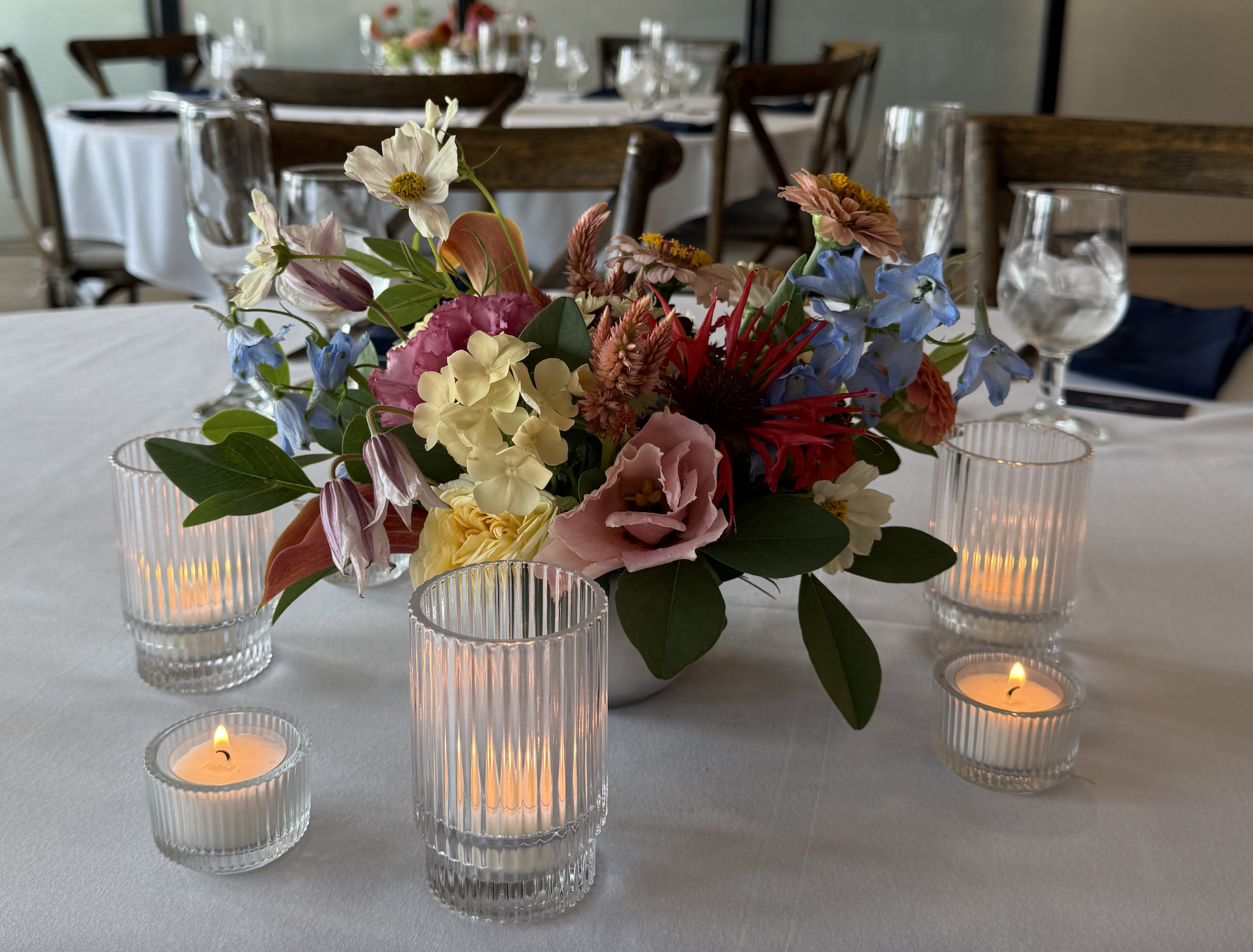 a colorful round table centerpiece on a table with white linens and candles