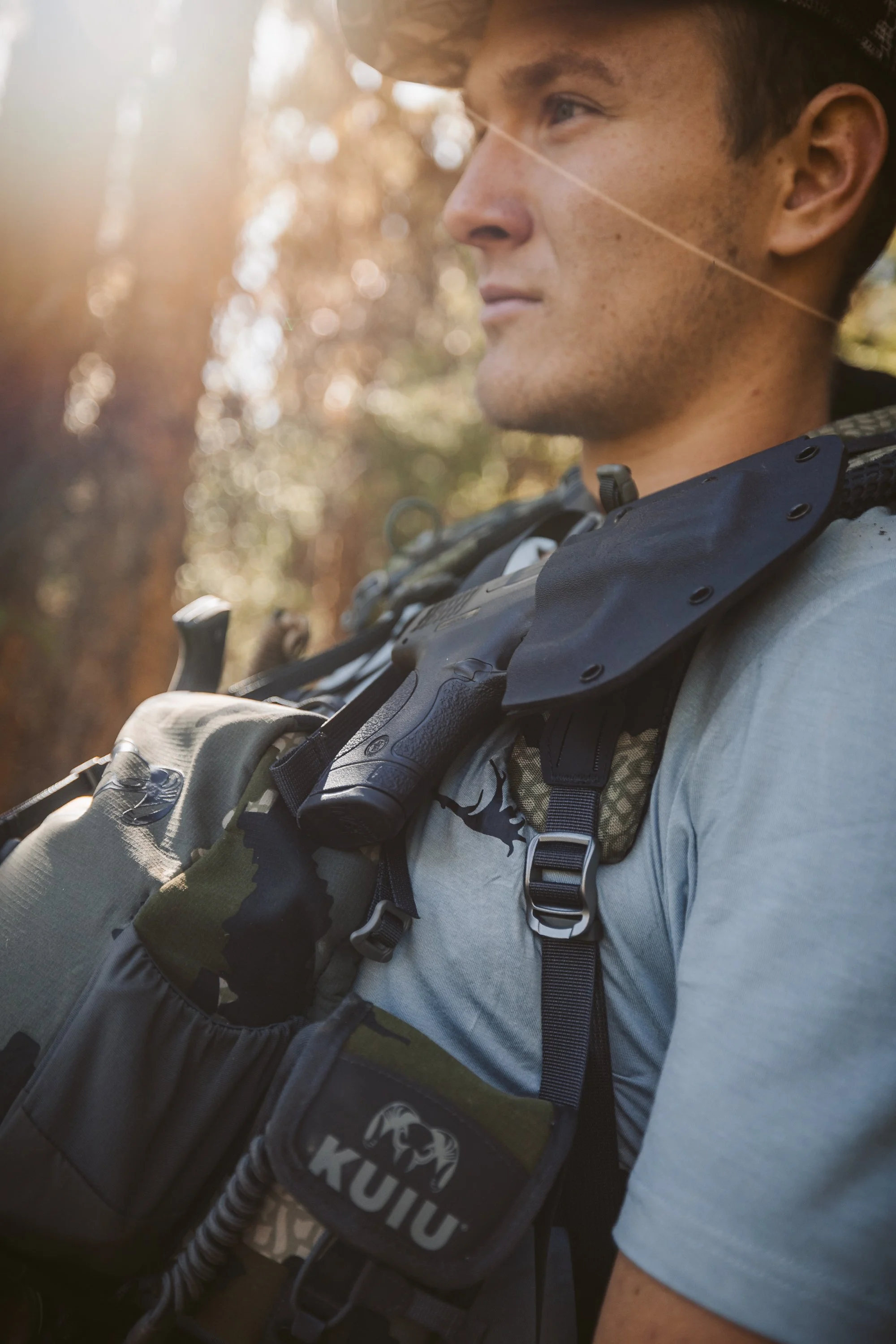 Close-up of a person outdoors wearing a backpack and a holstered gun.