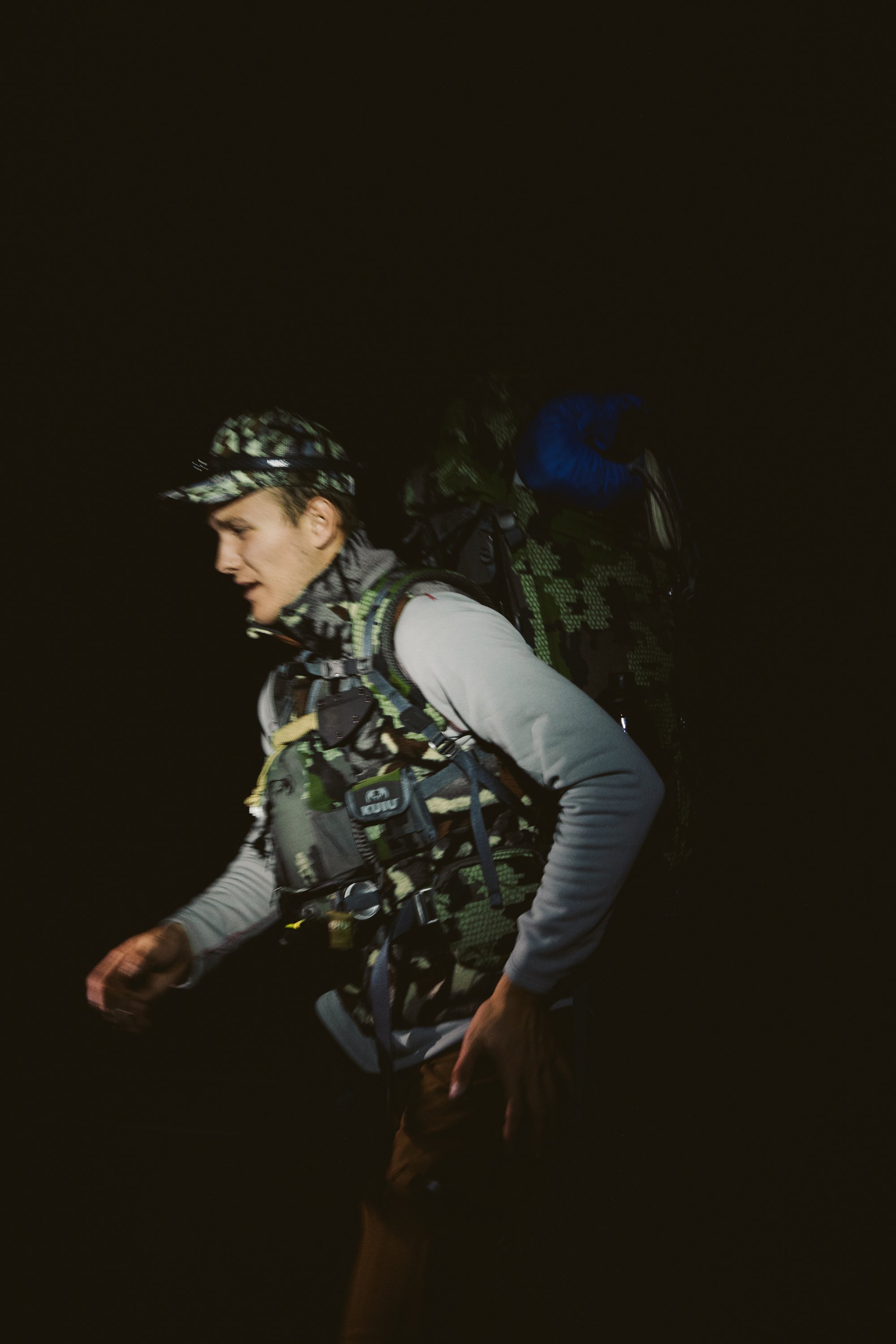 Person in camouflage gear with backpack at night.