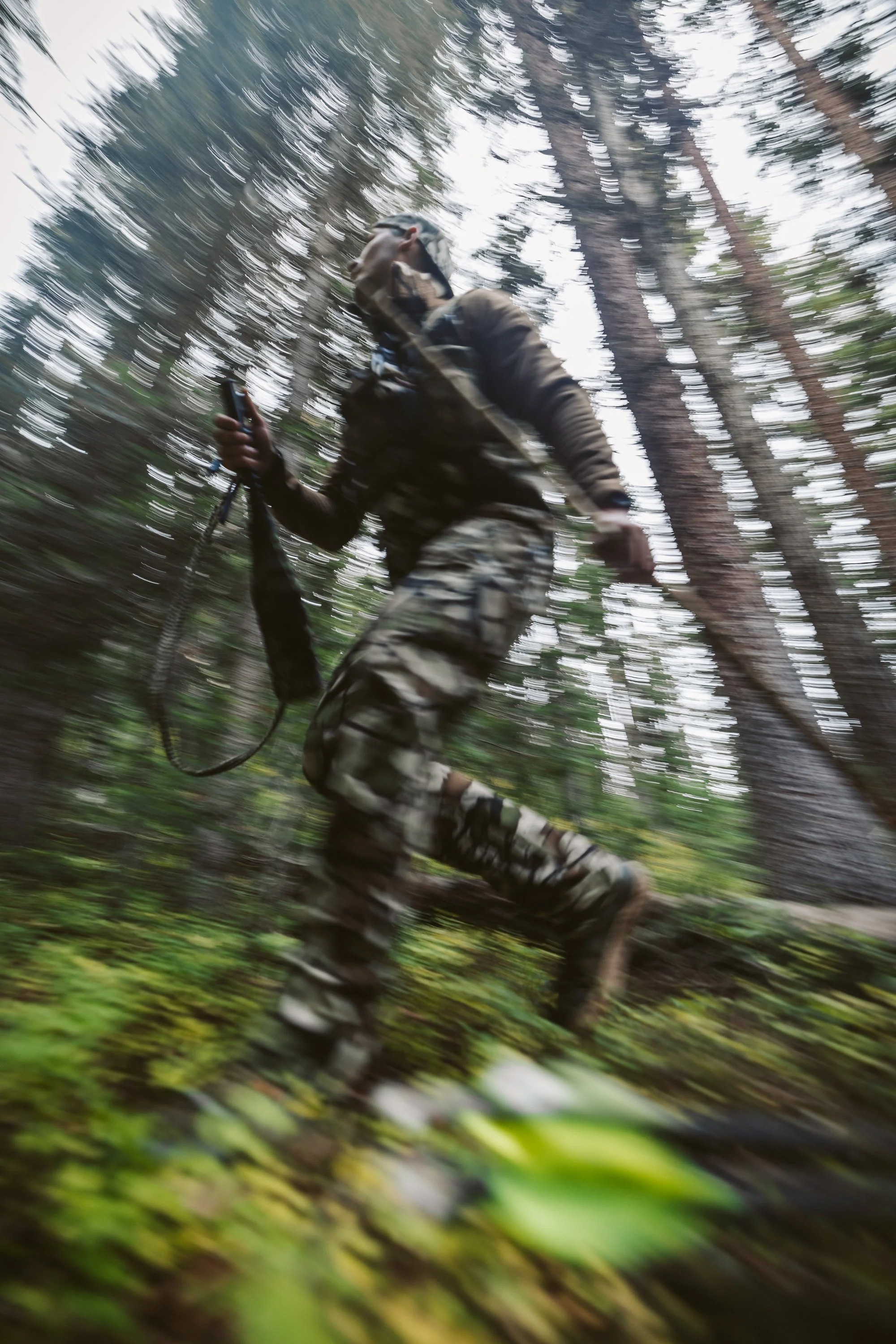 Blurry image of a person in camouflage running through a forest.