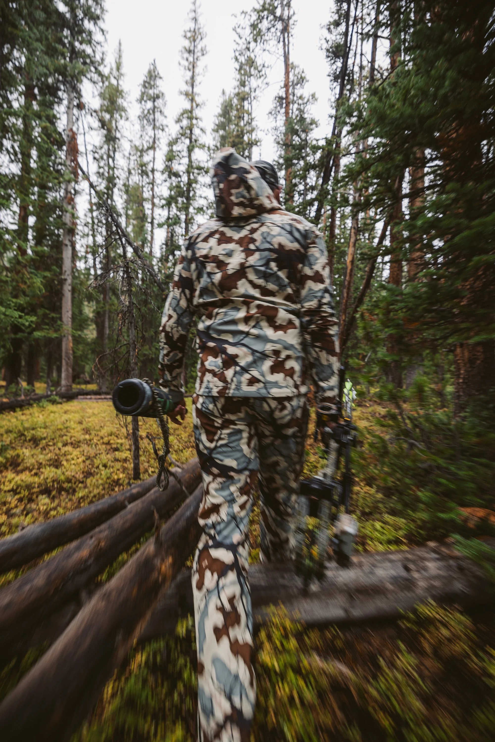 Person in camouflage carrying a camera and tripod in a forest
