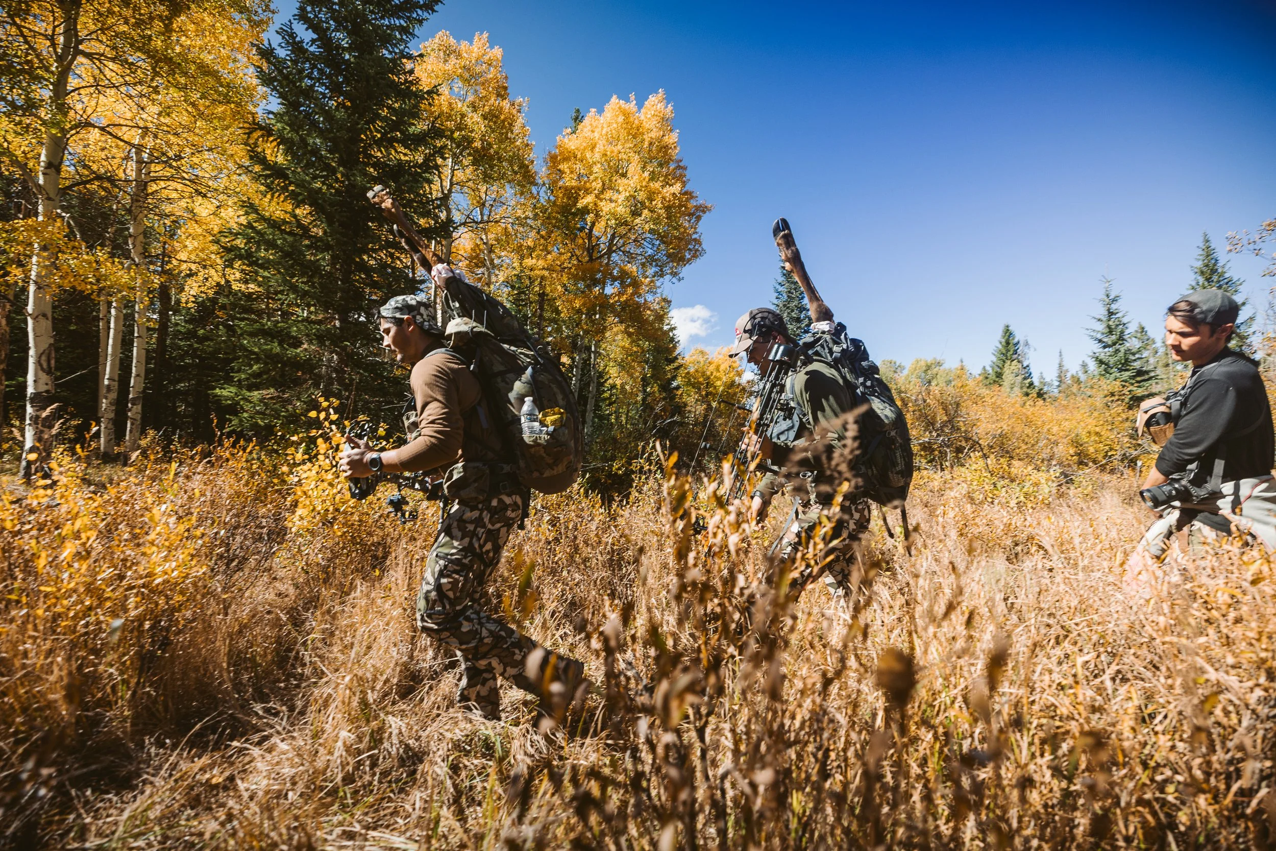 Three hunters walking through autumn forest with backpacks and gear
