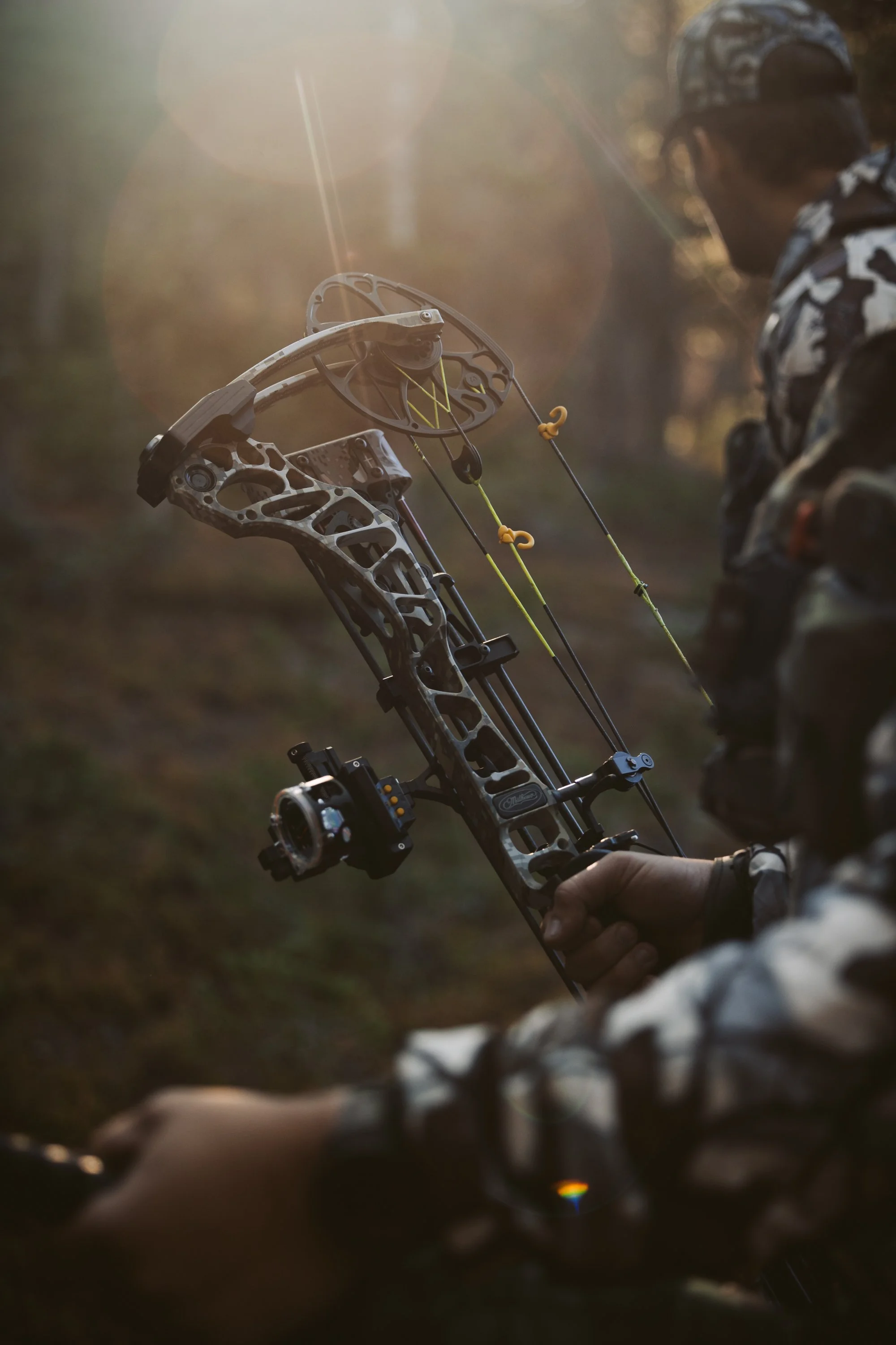 Person in camouflage gear holding a compound bow in a forest setting.