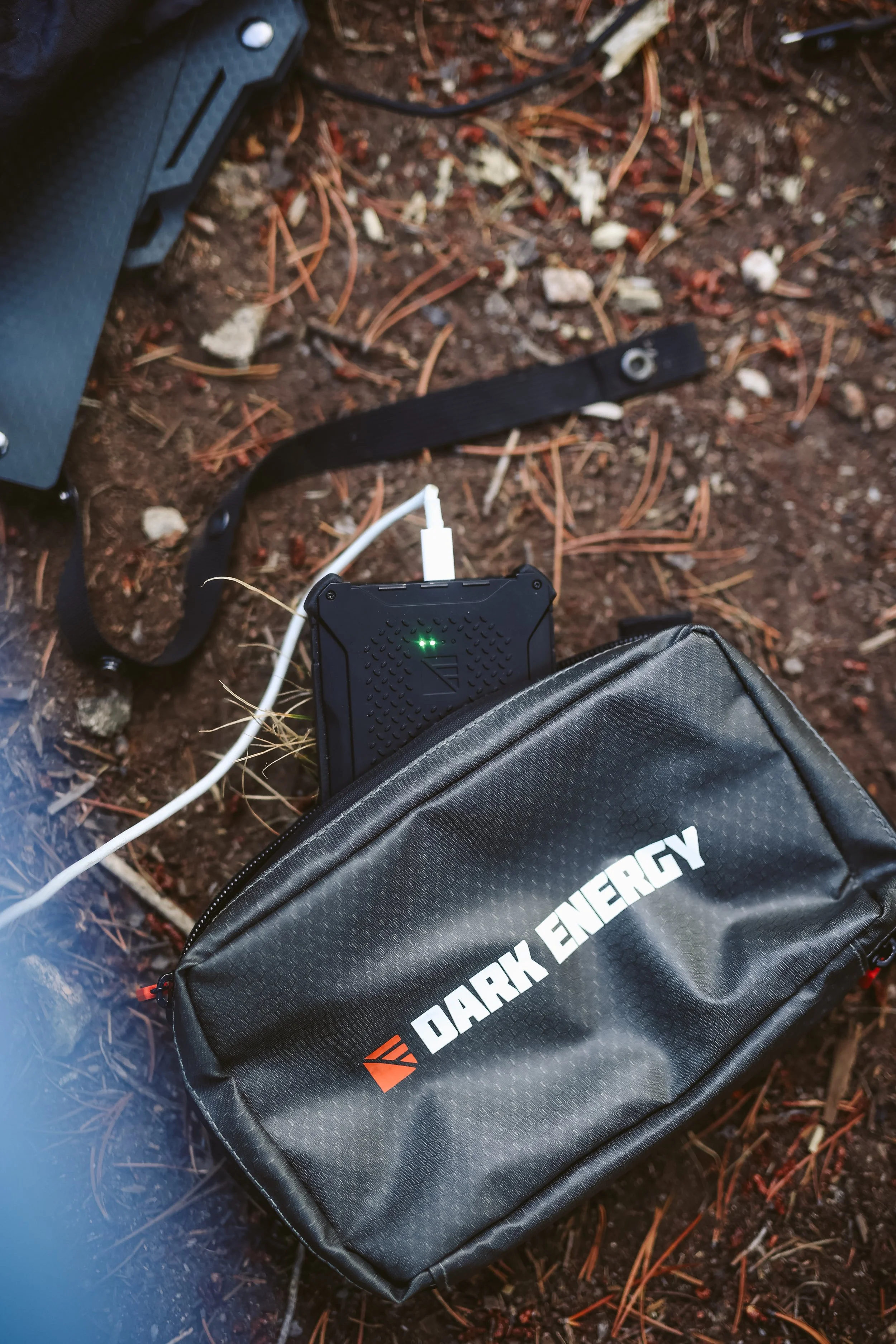 Black carrying case labeled "Dark Energy" with charging device on forest floor.