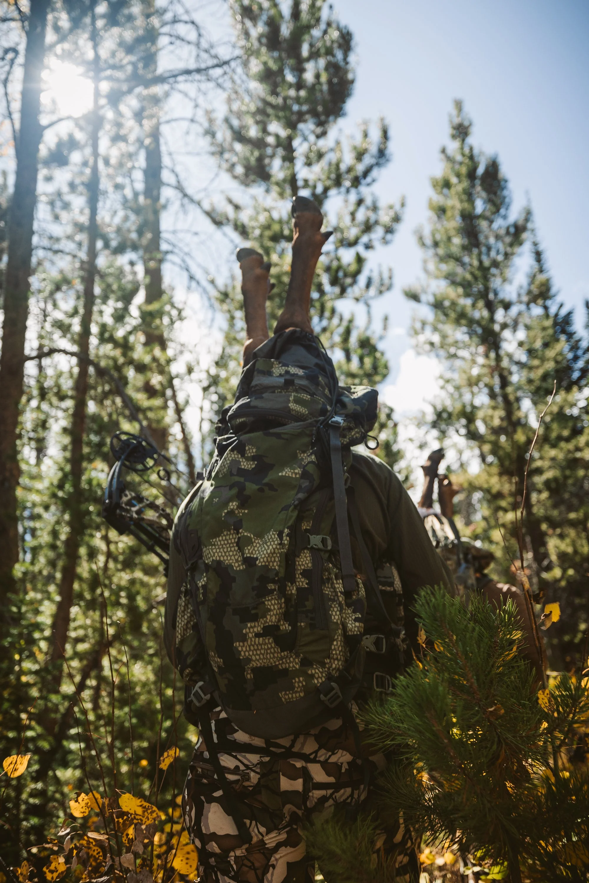 Hunter with camouflage gear carrying deer legs in a forest