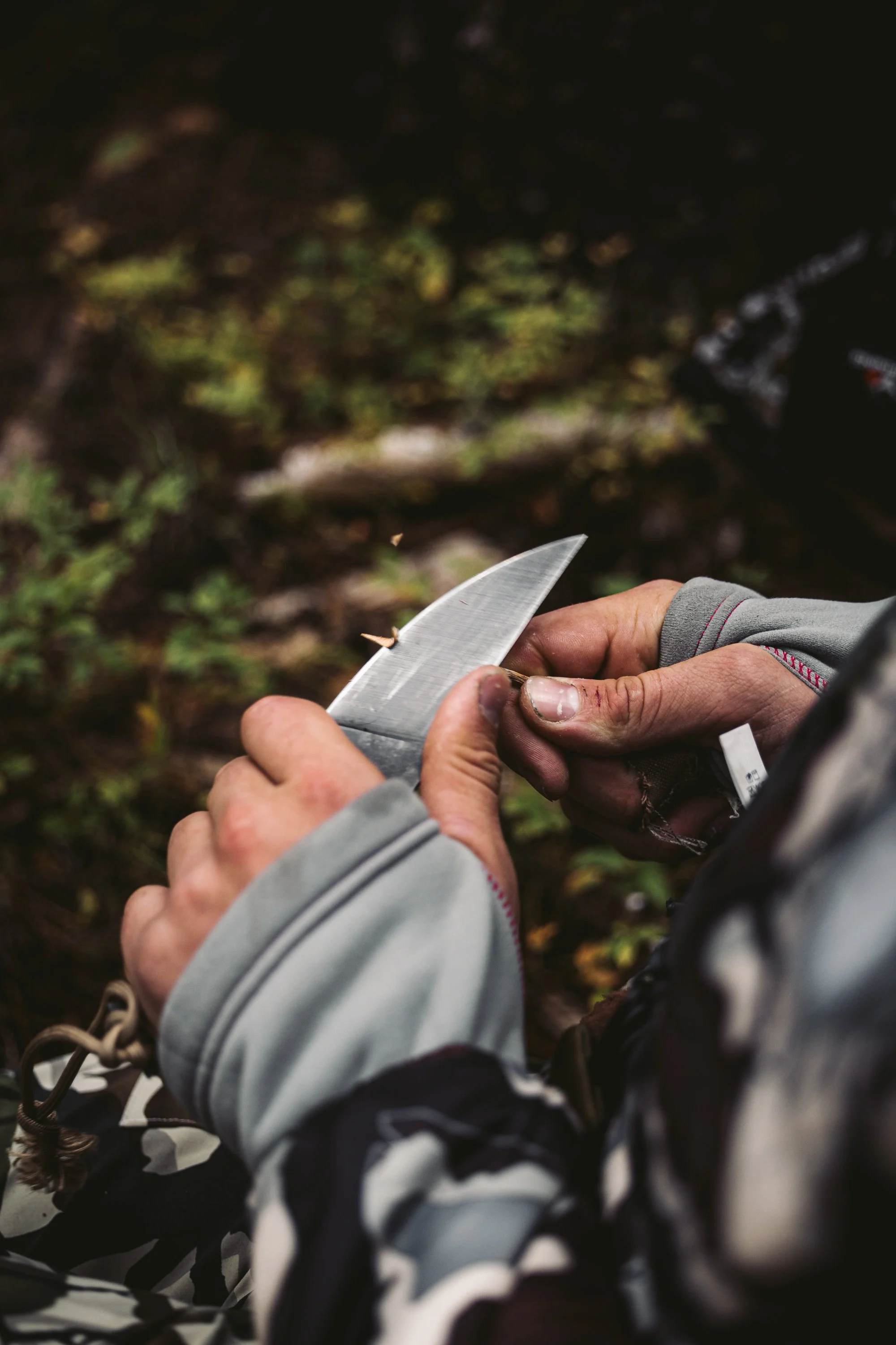 Person holding a knife in an outdoor setting with blurred foliage in the background.