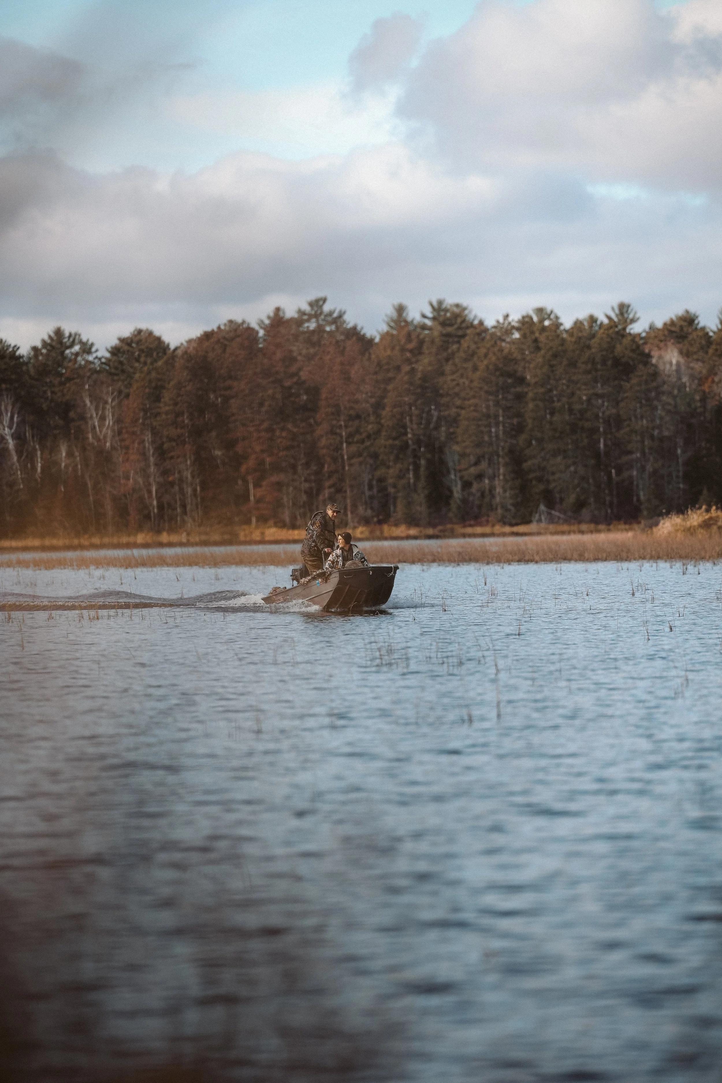Two people in a small boat on a lake with a forested shoreline in the background.