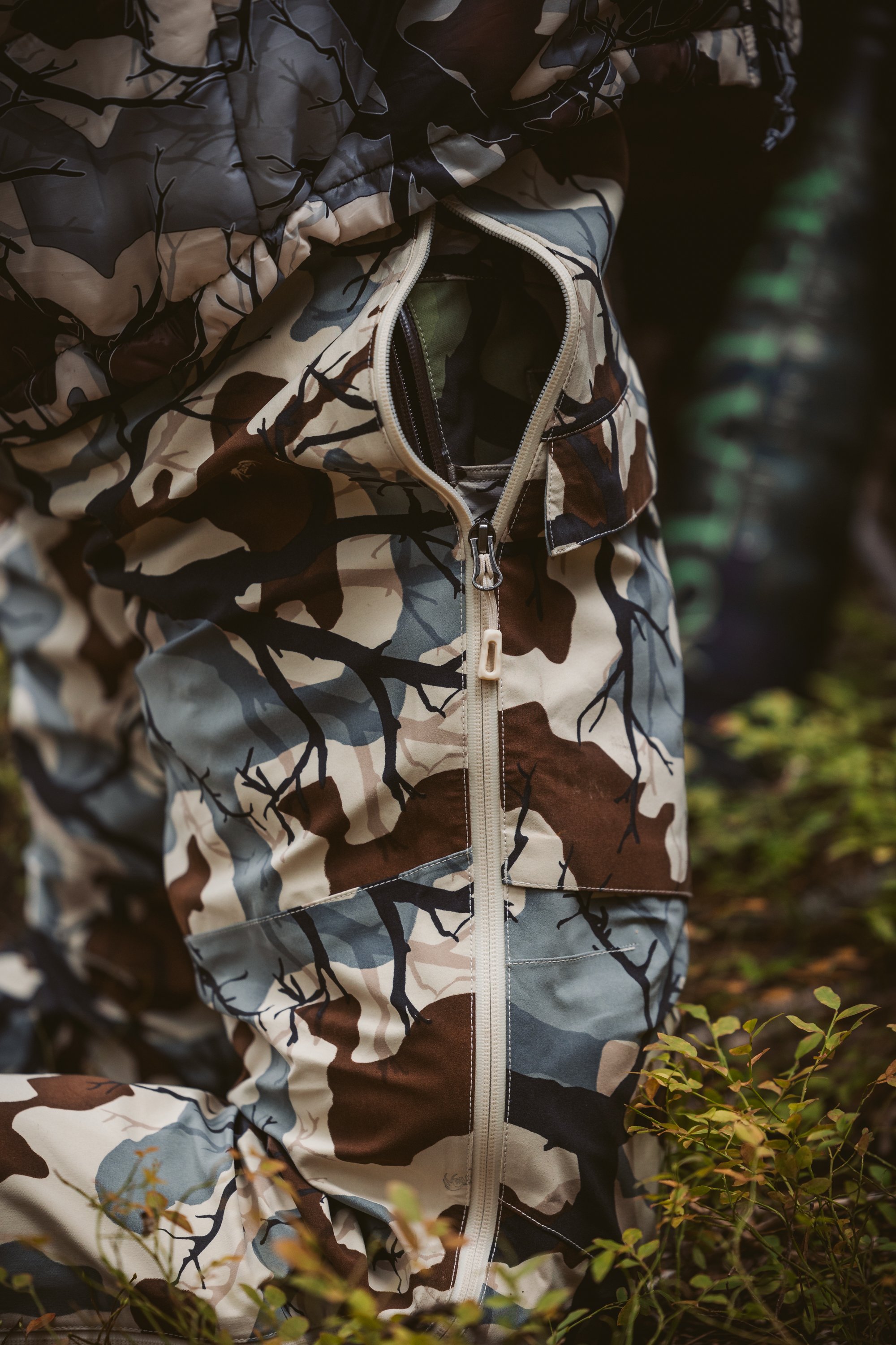 Close-up of camouflage clothing with a zipper partially open, surrounded by greenery.