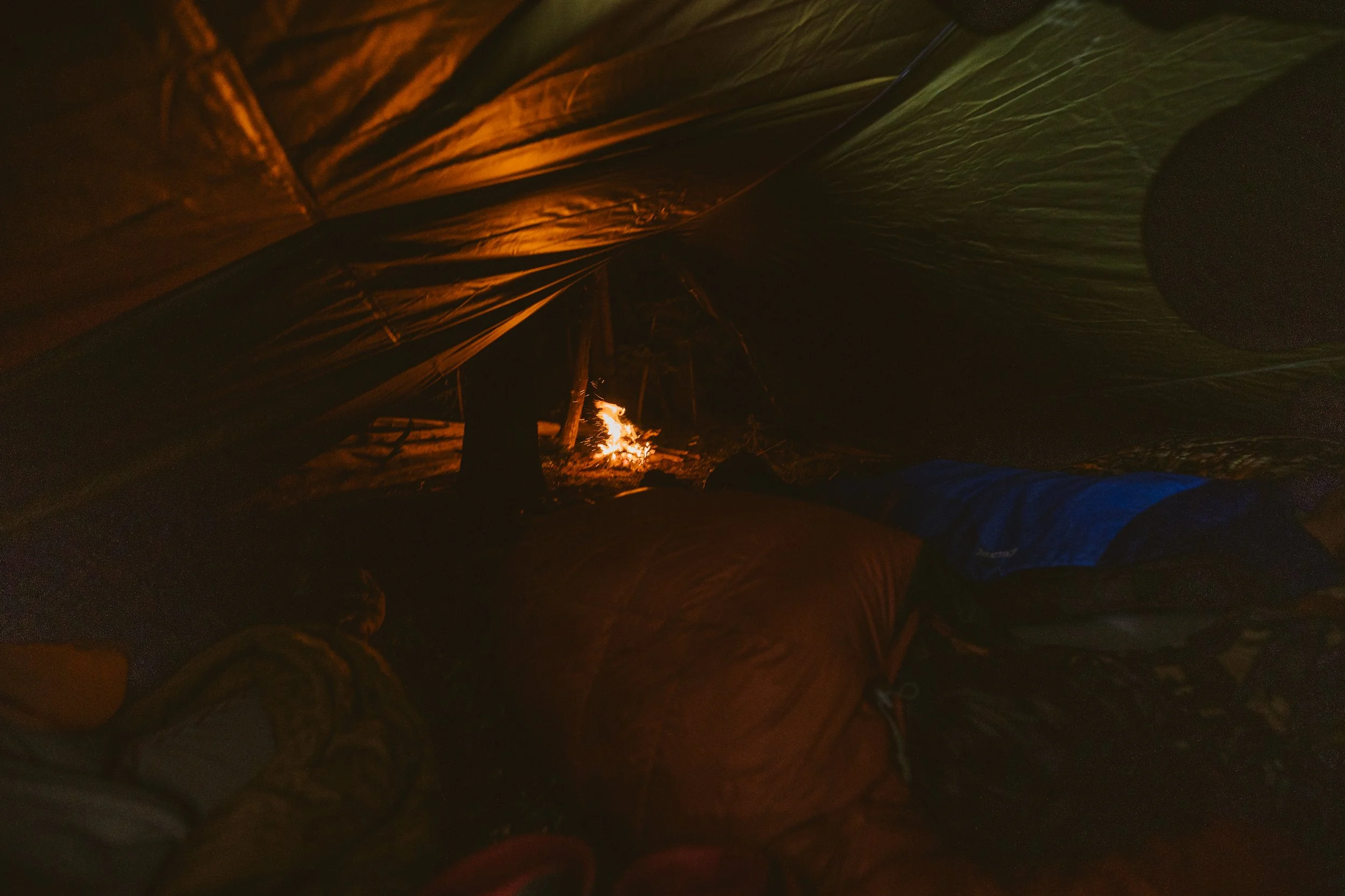 Inside a tent at night with campfire outside, sleeping bags and shadows visible.