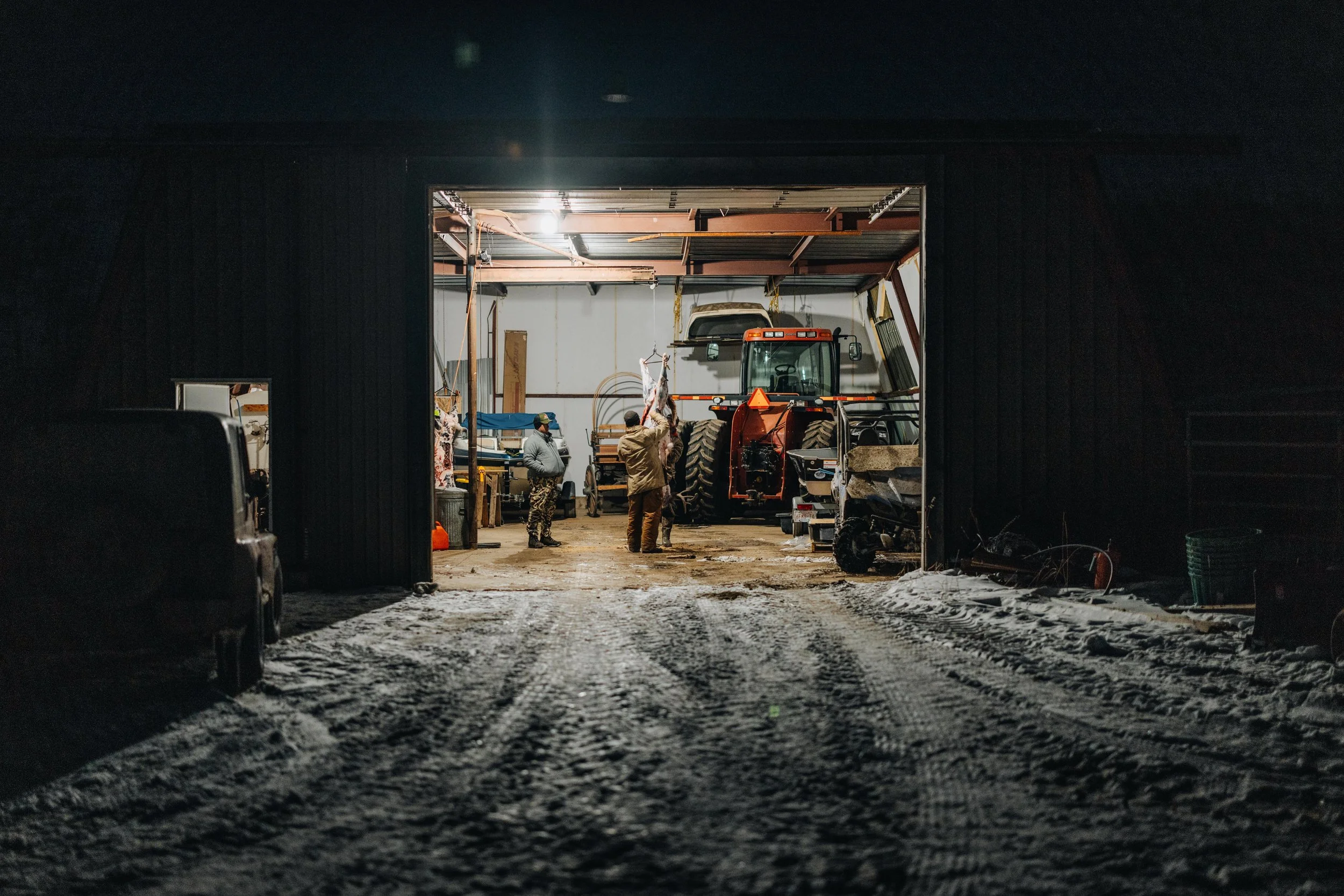 Interior of a barn at night with a tractor and people working inside.